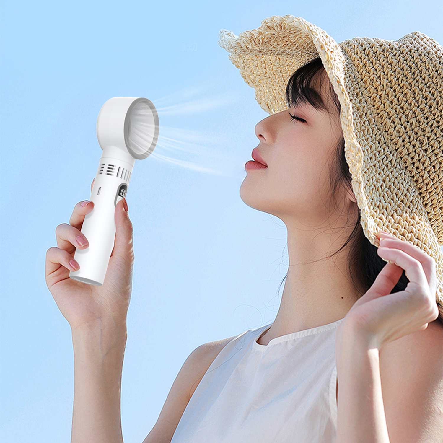 Una donna con cappello di paglia tiene in mano un ventilatore bianco, dirigendo l'aria verso il viso sotto un cielo blu.