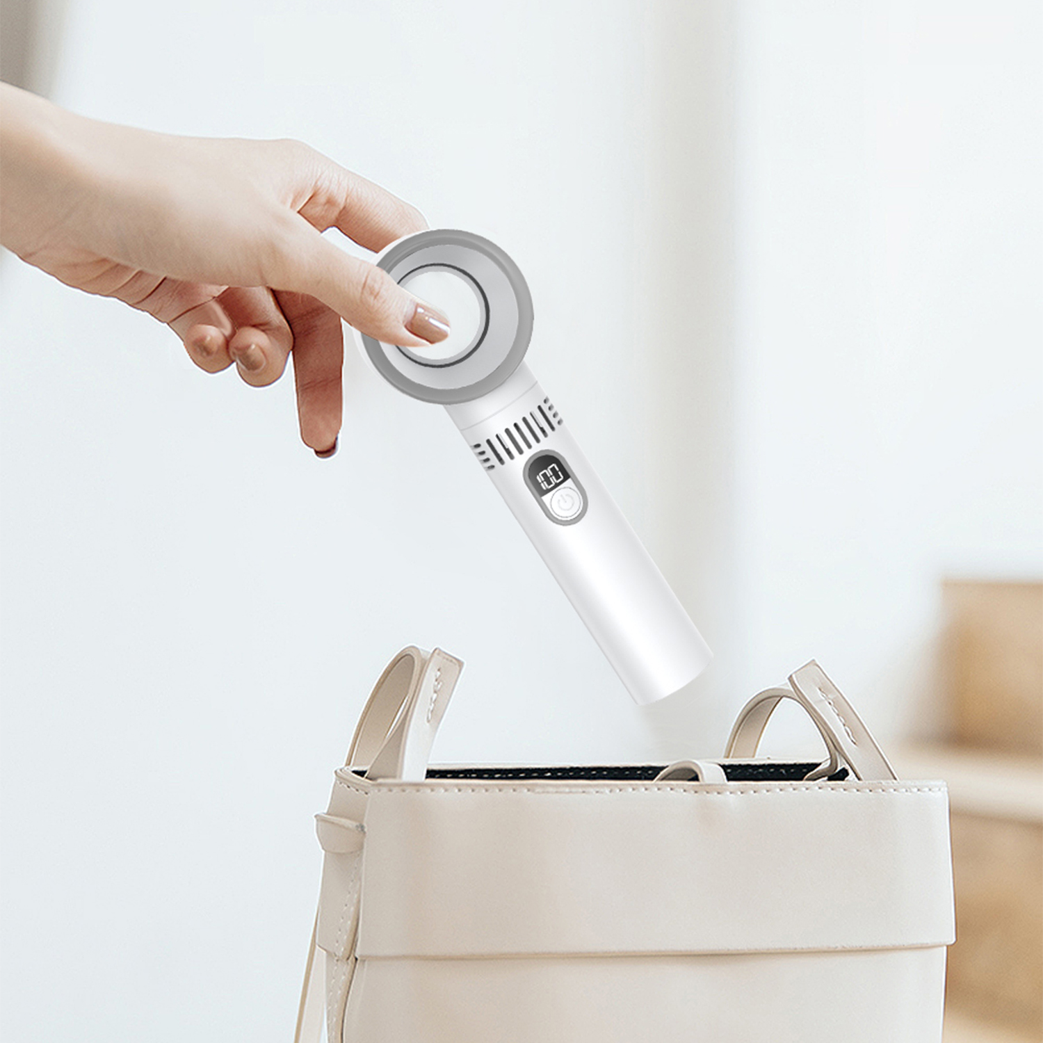 Una mano mette un dispositivo bianco in una borsa beige. Il dispositivo ha un display digitale e una parte superiore circolare.