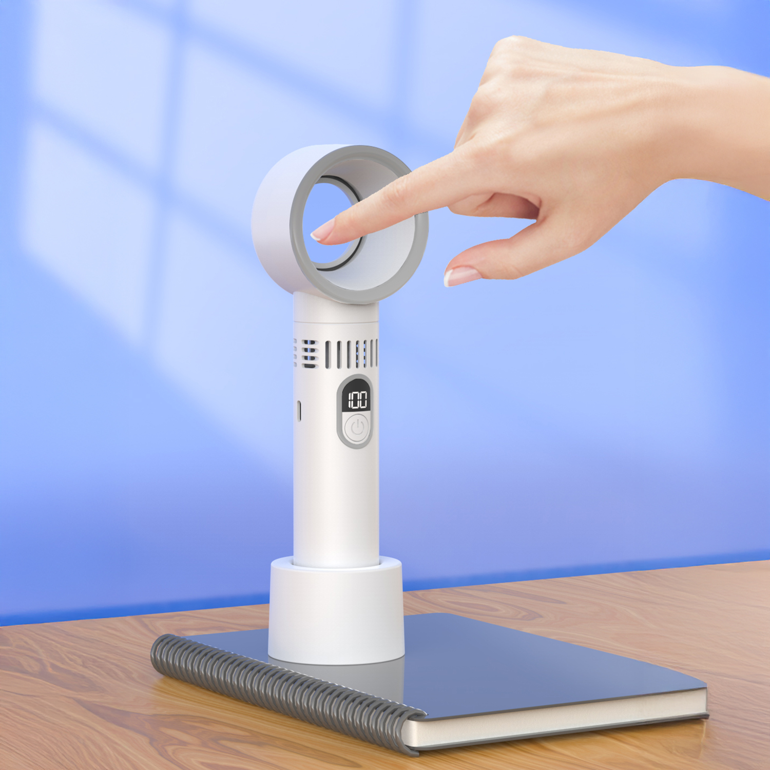 Una mano tocca un ventilatore bianco senza pale. Il ventilatore è su un tavolo di legno con un quaderno. Sfondo blu.