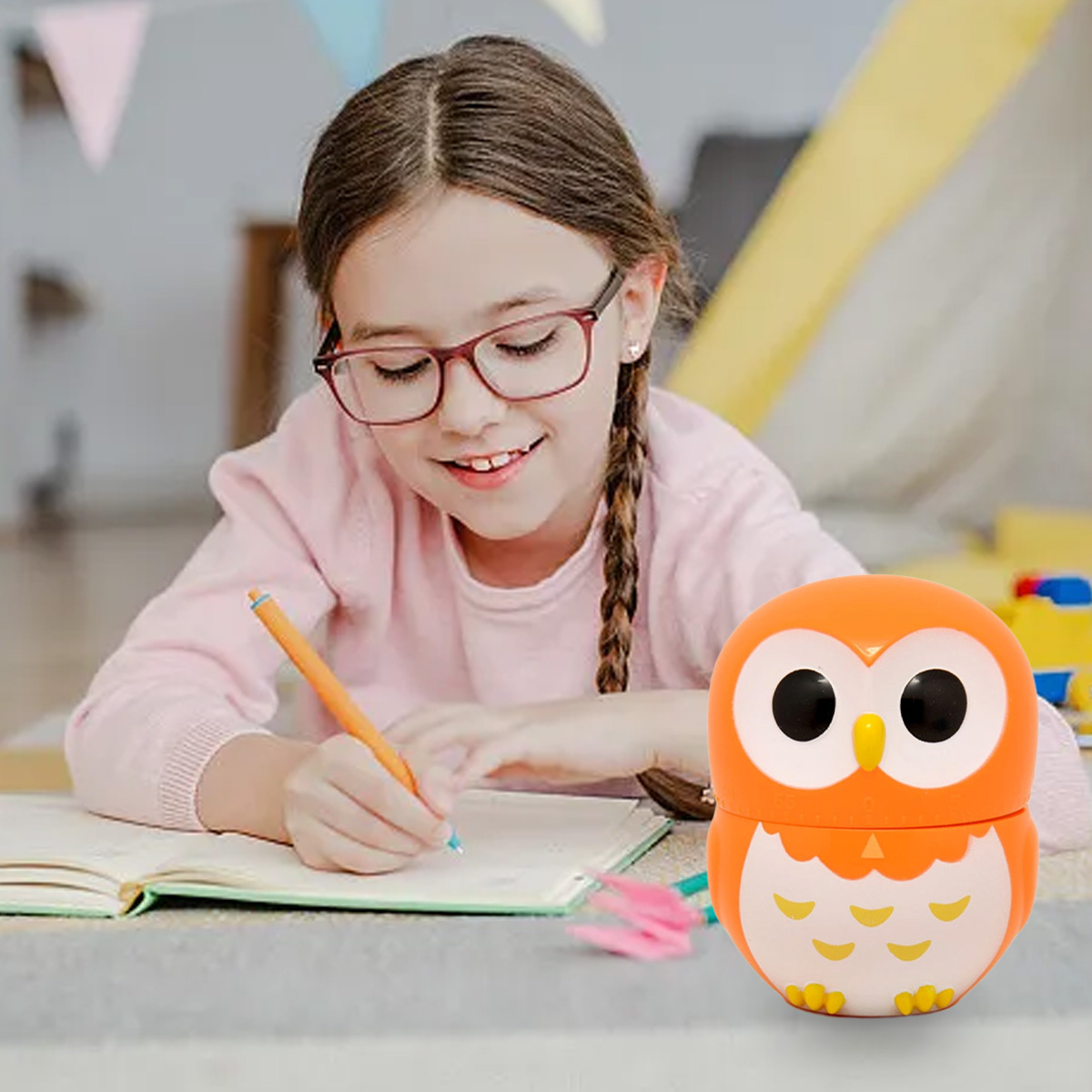Ein Mädchen mit Brille schreibt in ein Notizbuch, ein orangefarbener Eulen-Timer steht auf dem Tisch. Im Hintergrund gibt es bunte Dekorationen.