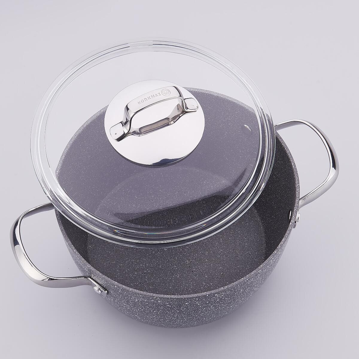 Een grijs gespikkelde pot met een glazen deksel en zilveren handvat. Het deksel staat een beetje open. De achtergrond is een wit oppervlak.