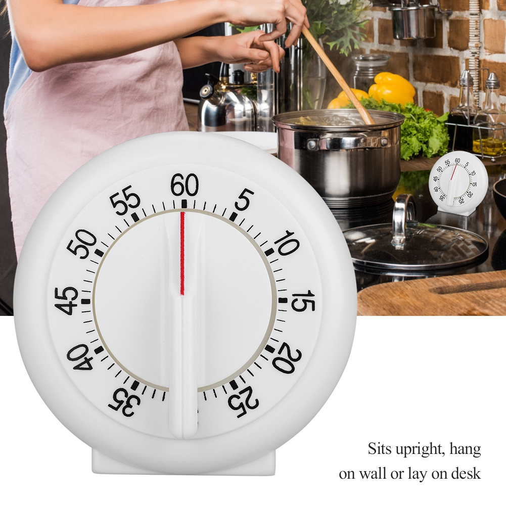 Ein weißer Küchentimer auf 60 Minuten eingestellt. Eine Person rührt Essen in einem Topf. Andere Töpfe, Gemüse und ein kleiner Timer sind vorhanden.