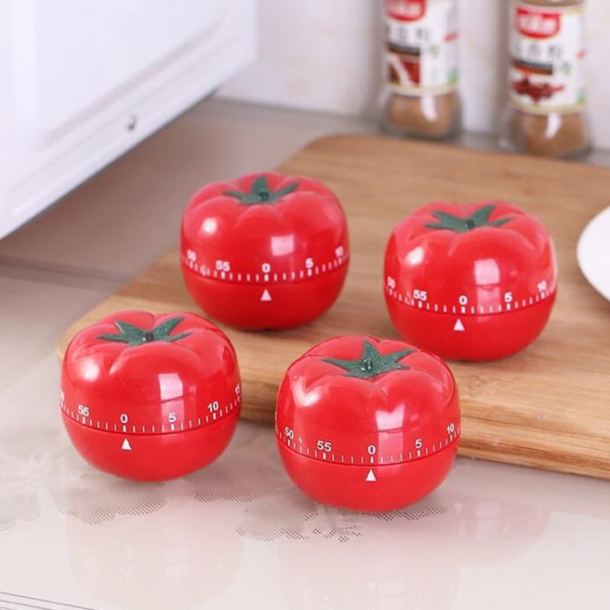 Vier rote, tomatenförmige Küchentimer auf einem Holzbrett. Jeder Timer hat eine grüne Oberseite und ein weißes Zifferblatt.