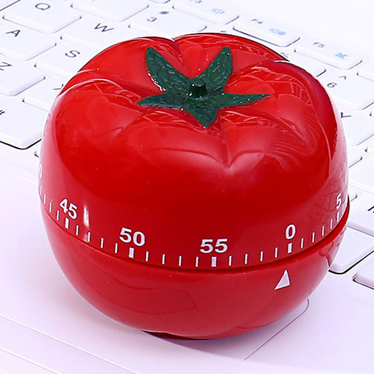 Ein roter tomatenförmiger Küchenwecker mit grünen Blättern liegt auf einer weißen Tastatur. Zahlen zeigen die Zeitschritte an.