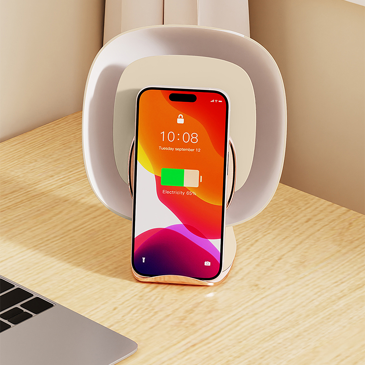 iPhone auf kabellosem Ladegerät, das Zeit und Akku anzeigt. Das Ladegerät steht auf einem Holztisch. Links ist ein Laptop.