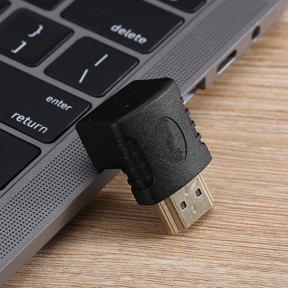 Schwarzer HDMI-Adapter, der an einen Laptop angeschlossen ist und auf einer Holzoberfläche liegt. Tasten wie 'Return' und 'Delete' sind sichtbar.