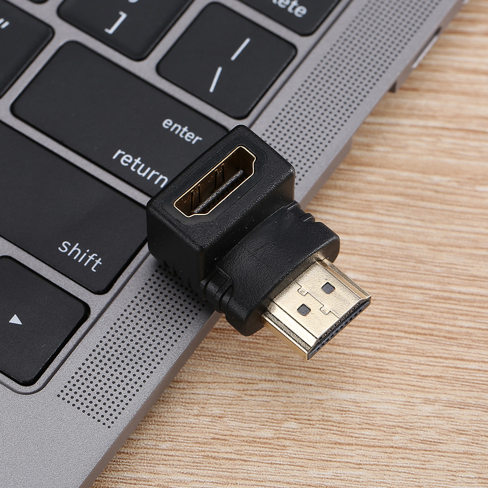 Schwarzer HDMI-Adapter auf einer Laptop-Tastatur. Der Adapter ist abgewinkelt und hat goldene Anschlüsse. Die Tastatur hat schwarze Tasten und eine graue Oberfläche.