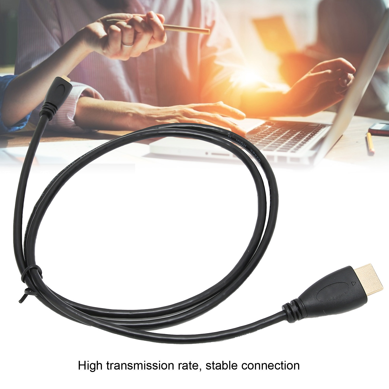Schwarzes HDMI-Kabel mit Steckern. Im Hintergrund sind Hände in der Nähe eines Laptops. Text: Hohe Übertragungsrate, stabile Verbindung.