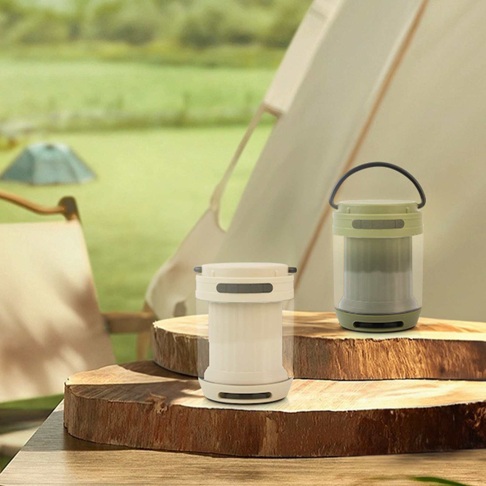 Zwei Campinglampen stehen auf einer Holzoberfläche. Eine ist weiß, die andere grün. Im Hintergrund sind ein Zelt und Gras.