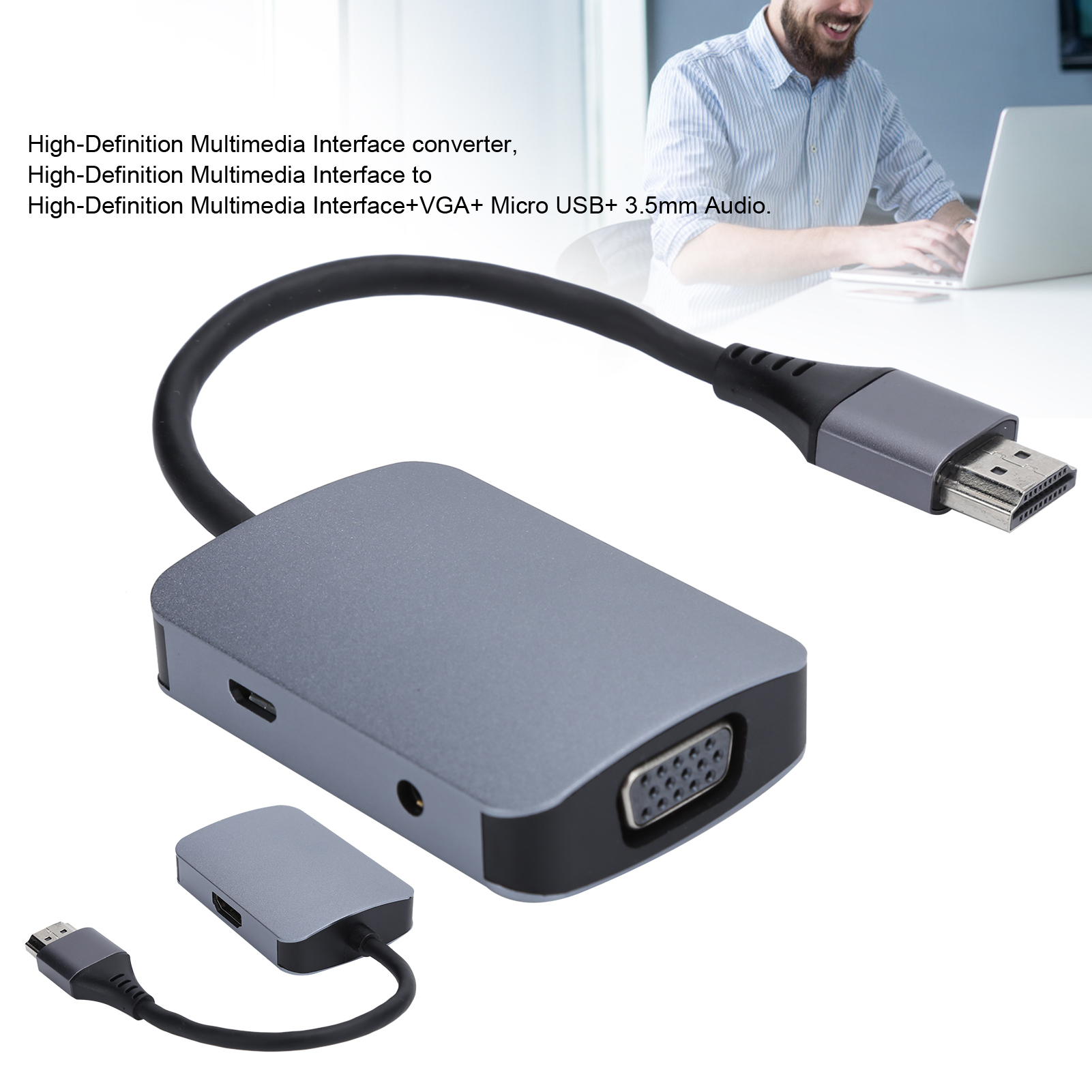 Grauer HDMI-Adapter mit schwarzem Kabel, VGA-Anschluss und kleinerem Adapter. Im Hintergrund arbeitet ein Mann an einem Laptop.