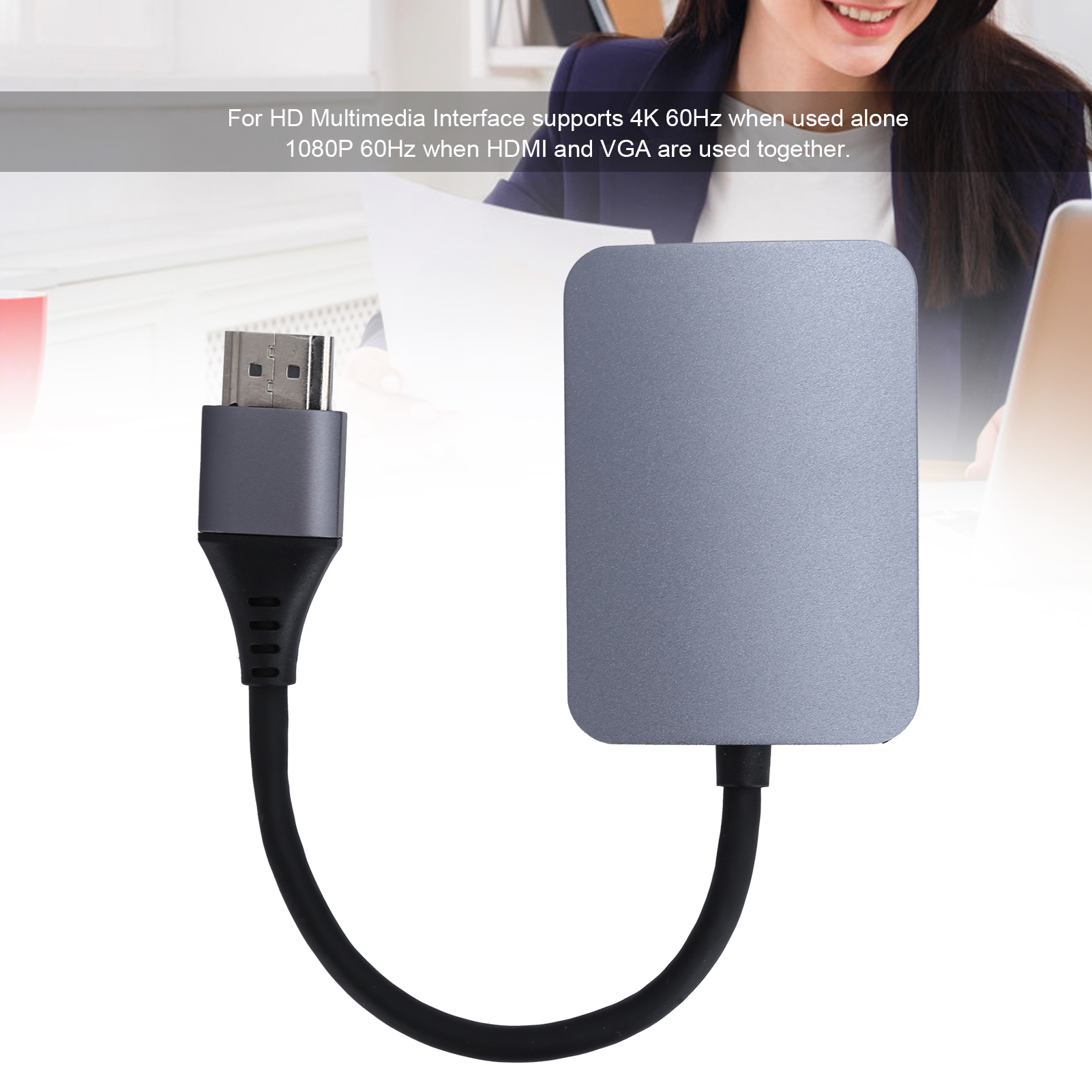 Grauer HDMI-Adapter mit schwarzem Kabel. Im Hintergrund arbeitet eine Person.