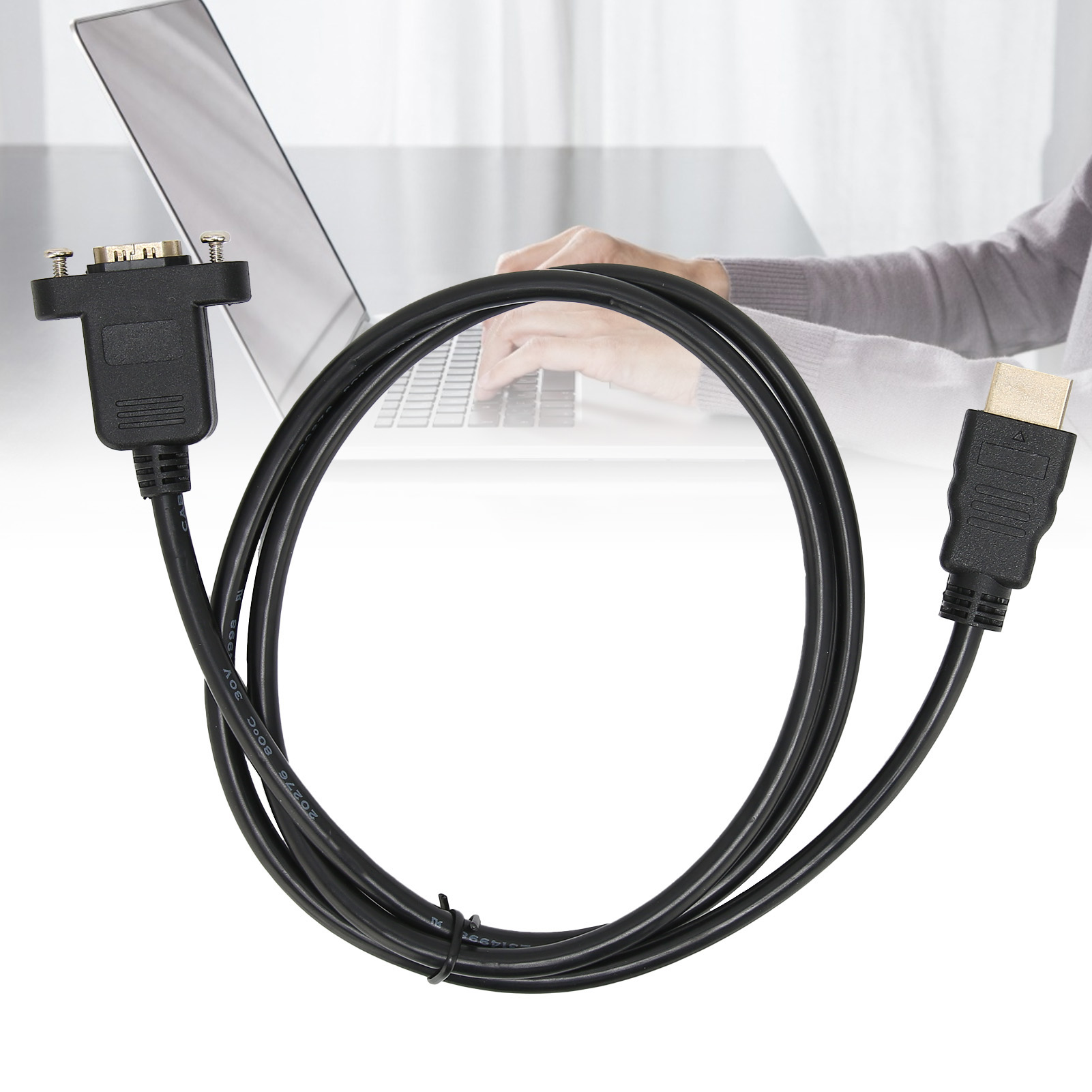 Schwarzes HDMI-zu-VGA-Kabel mit Anschlüssen. Im Hintergrund verschwommen eine Person mit einem Laptop.