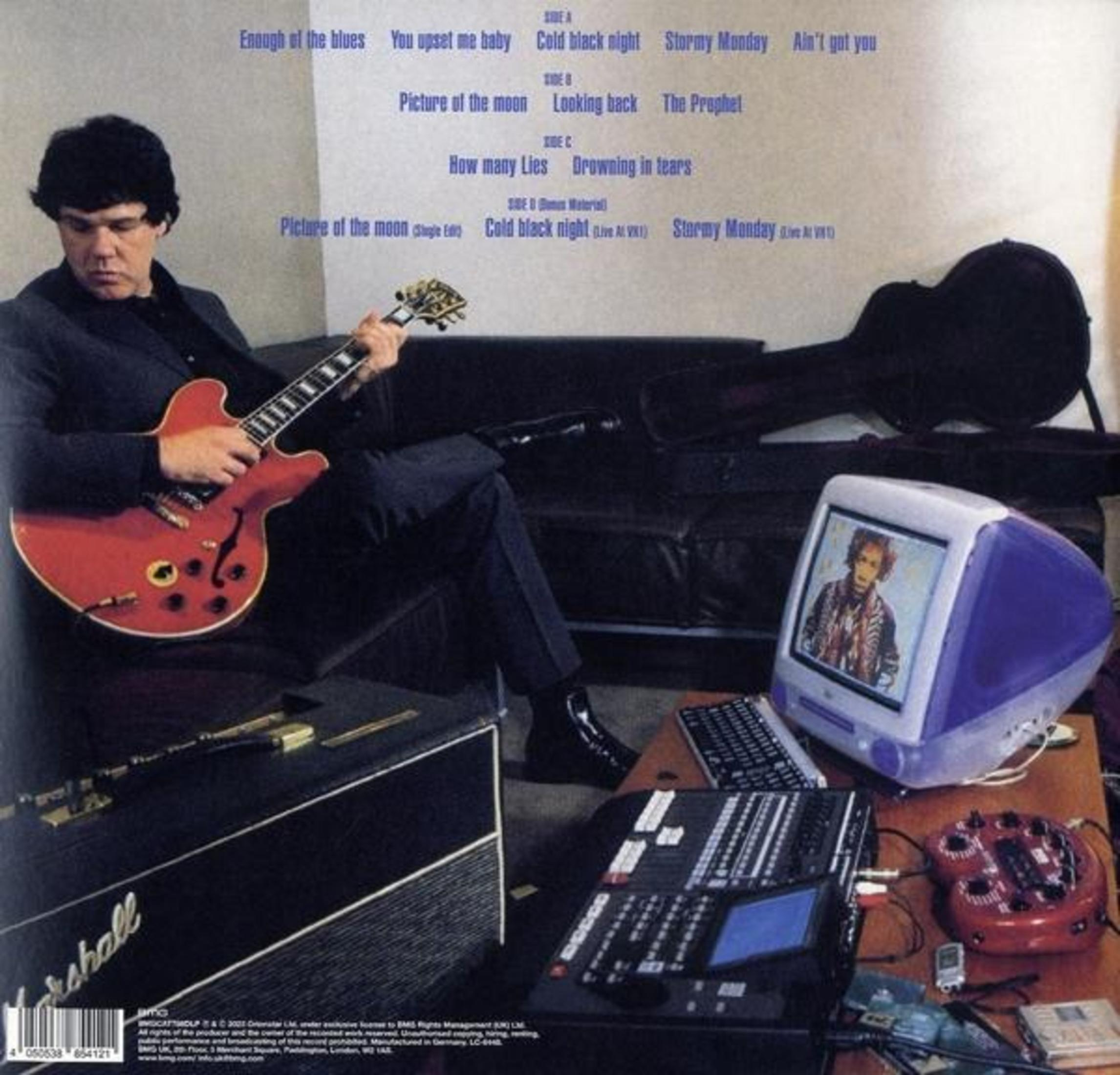 Uomo suona chitarra rossa, seduto. Un monitor mostra una persona. C'è un mixer e un'unità effetti rossa. Una custodia per chitarra è dietro.