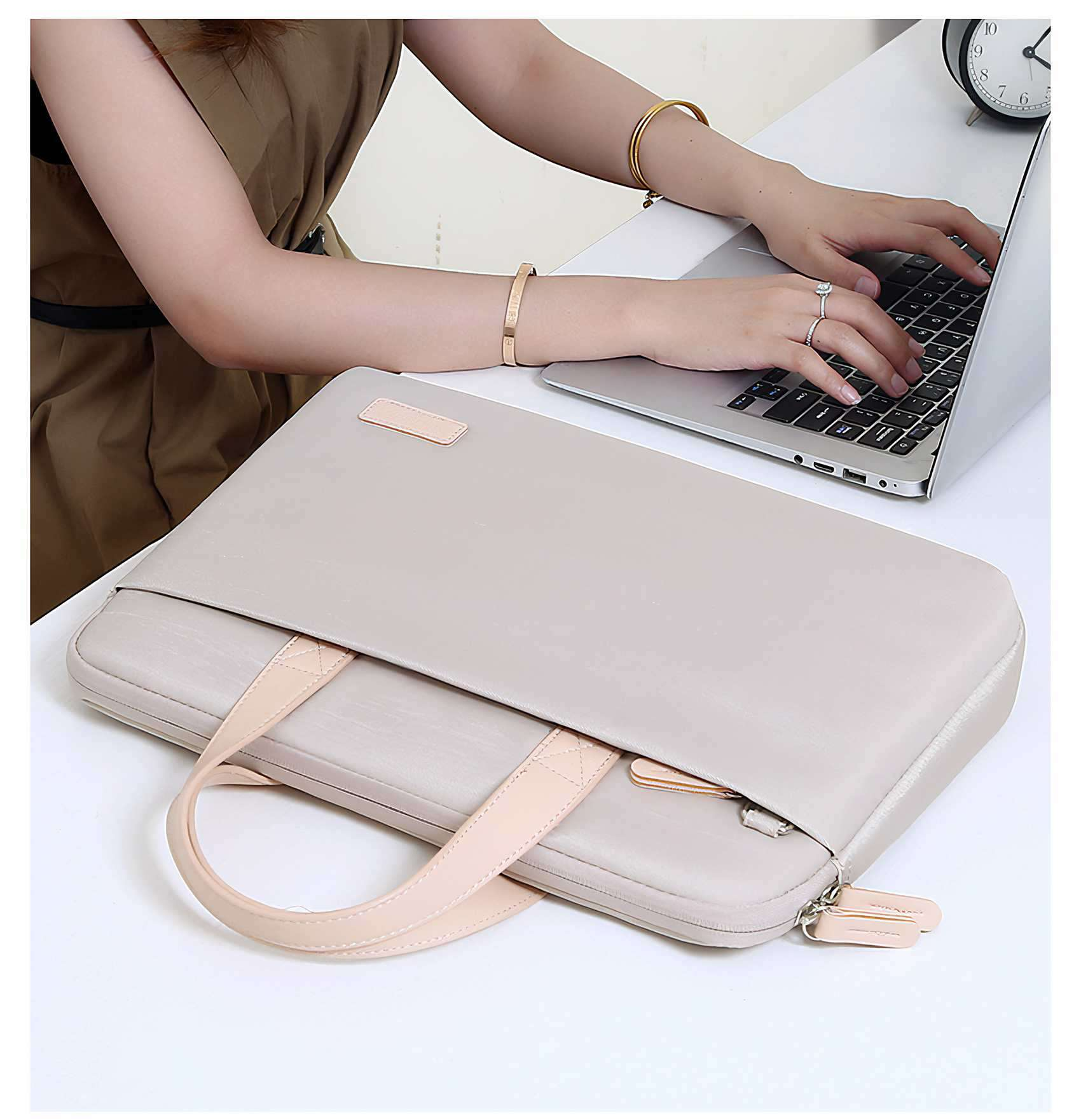 Eine Frau tippt auf einem Laptop. Es gibt eine Laptoptasche, eine Uhr und einen Ring an ihrem Finger. Im Hintergrund ist eine Uhr.