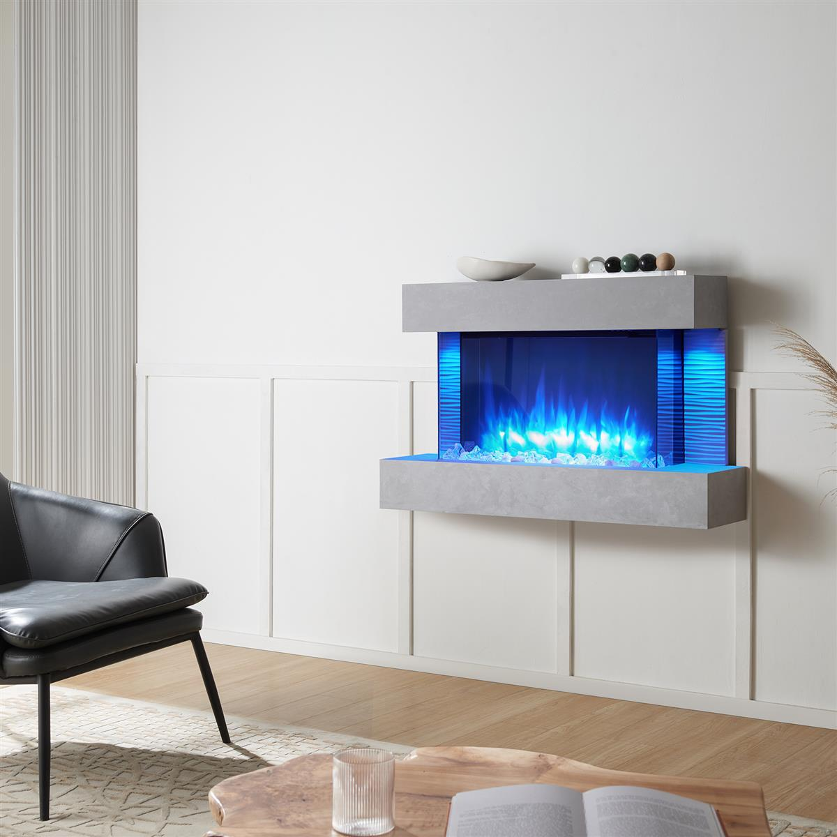 Ein moderner Kamin mit blauen Flammen ist an einer weißen Wand montiert. Davor stehen ein schwarzer Stuhl und ein Holztisch.