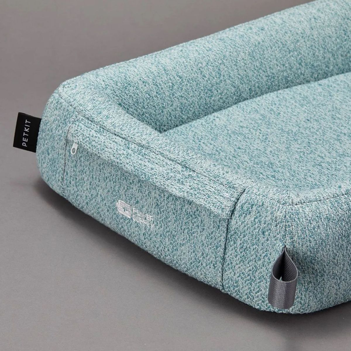 Un letto blu per animali domestici con superficie strutturata. Ha una forma arrotondata con bordo rialzato. Il letto ha una maniglia e un'etichetta con la scritta PETKIT.