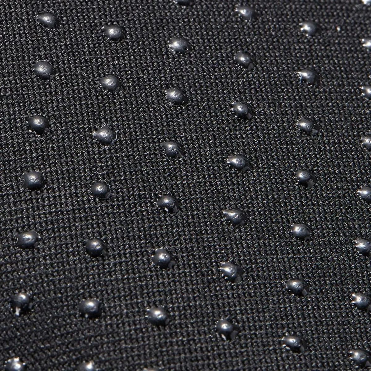 Primo piano di tessuto nero con molti piccoli rilievi arrotondati color argento. La trama suggerisce una superficie antiscivolo.
