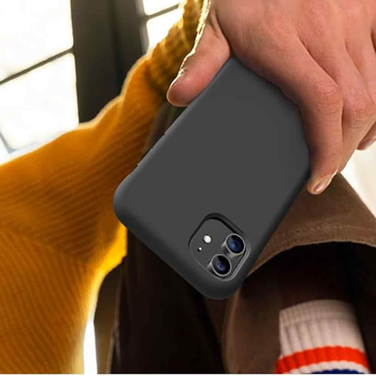 Eine Hand hält eine schwarze Handyhülle. Die Person trägt einen orangefarbenen Pullover, eine braune Hose und eine weiße Socke mit roten Streifen.