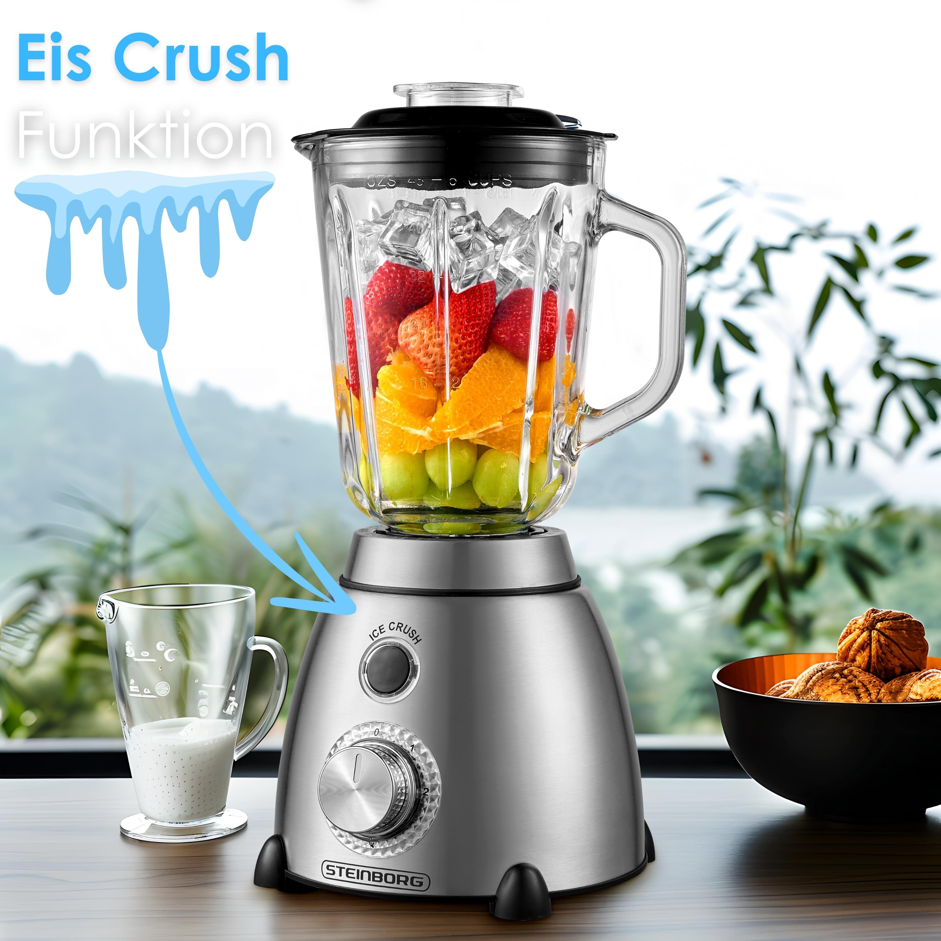 Mixer mit Früchten, Eis. Auf dem Tisch stehen ein Glas mit Flüssigkeit und eine Schüssel mit Nüssen. Der Hintergrund ist ein Fenster.