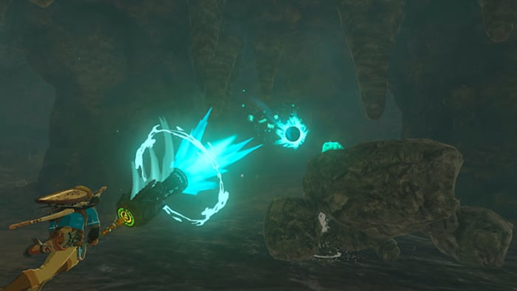 Un personaggio in abito blu sta sparando un raggio di energia blu brillante a un globo nero luminoso in una grotta. C'è una roccia a destra.