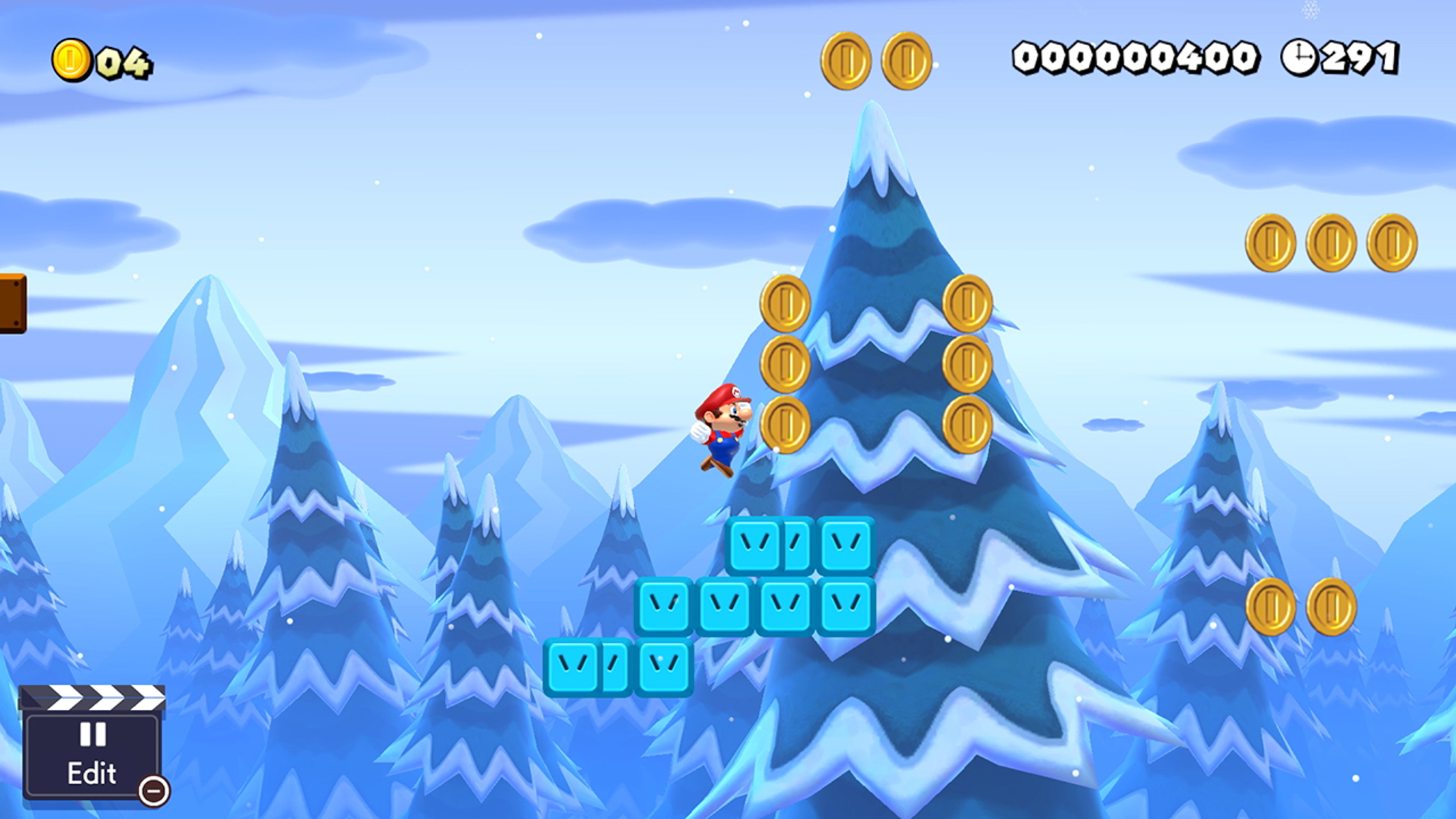 Mario springt über blaue Plattformen in einer schneebedeckten Szene. Goldmünzen sind verstreut, schneebedeckte Berge und Bäume bilden den Hintergrund.