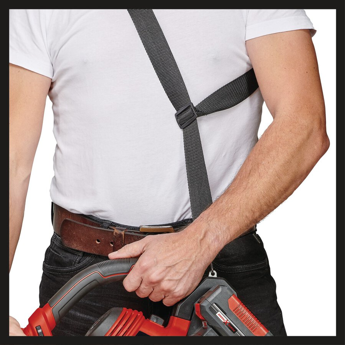 Ein Mann in einem weißen Hemd und einer schwarzen Hose hält ein rot-schwarzes Elektrowerkzeug. Er trägt einen Gurt über Brust und Schultern.