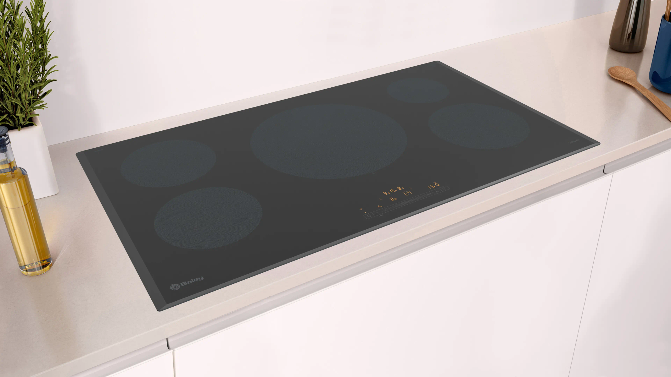 Czarna płyta indukcyjna z pięcioma strefami gotowania na białym blacie. Po lewej stronie butelka oleju i roślina.