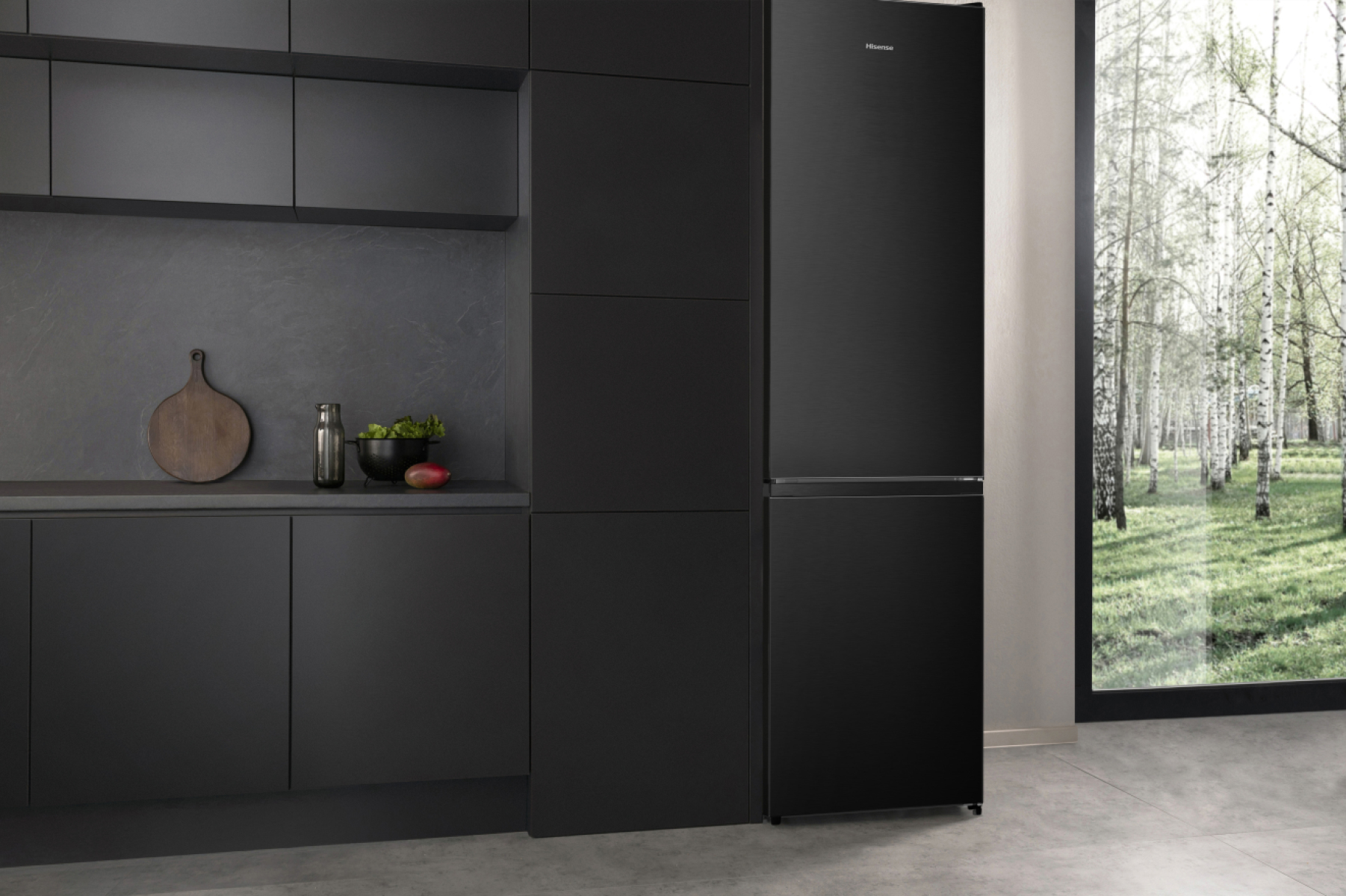 Eine schwarze Küche mit schwarzem Kühlschrank, Schränken und Arbeitsplatte. Ein rundes Schneidebrett, eine Vase und eine Schüssel stehen auf der Theke.