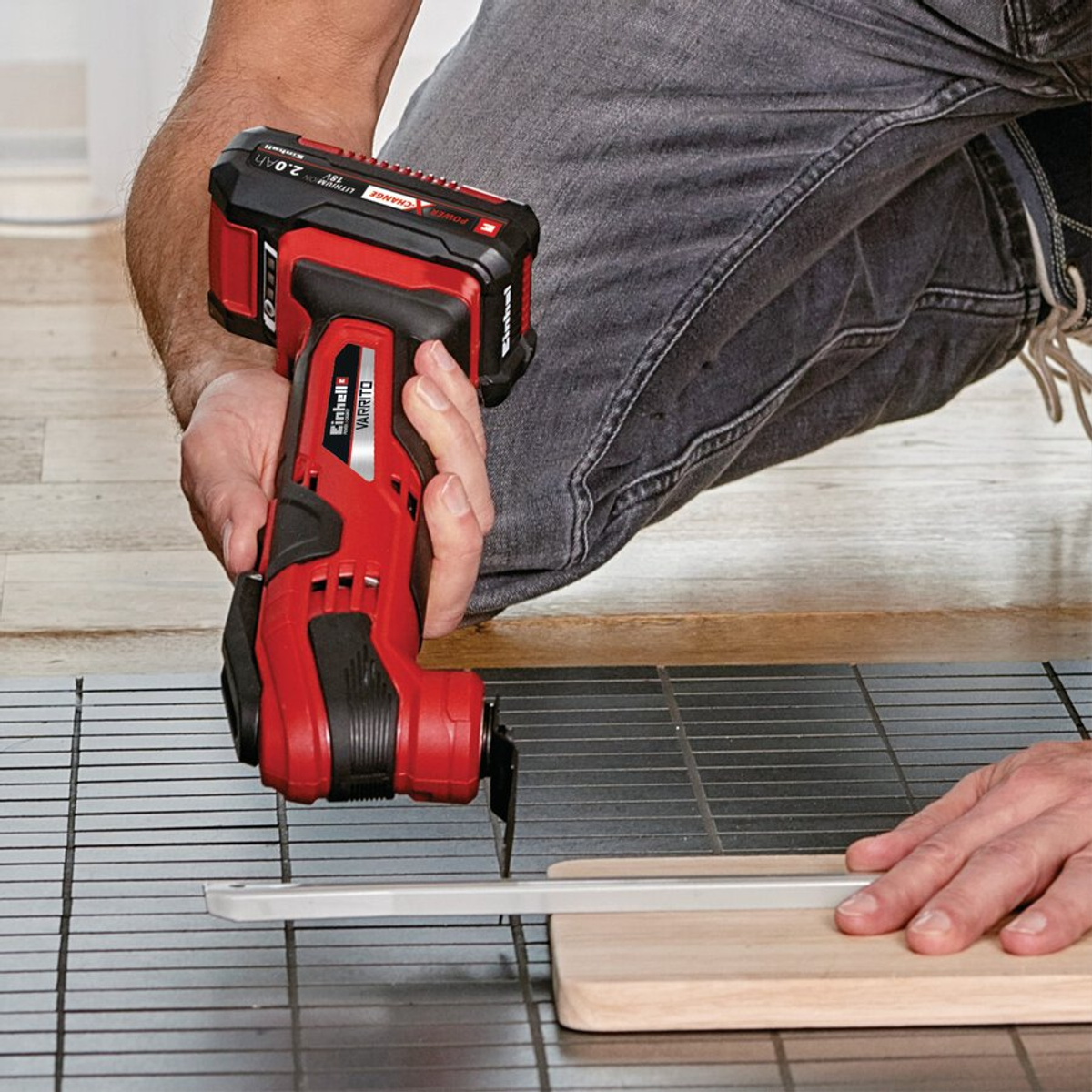 Eine Person benutzt ein rot-schwarzes Elektrowerkzeug, um ein Holzbrett zu schneiden. Das Werkzeug wird von einer Person in grauen Jeans gehalten.