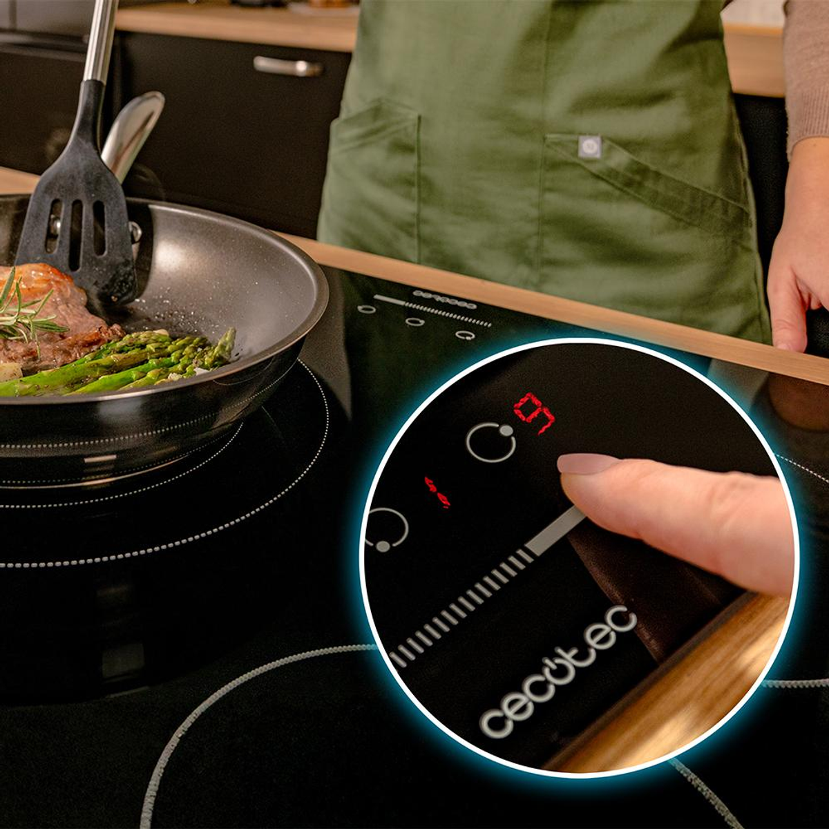 Osoba gotuje szparagi i mięso na patelni na czarnej płycie grzewczej. Panel sterowania płyty jest podświetlony palcem, który go dotyka.