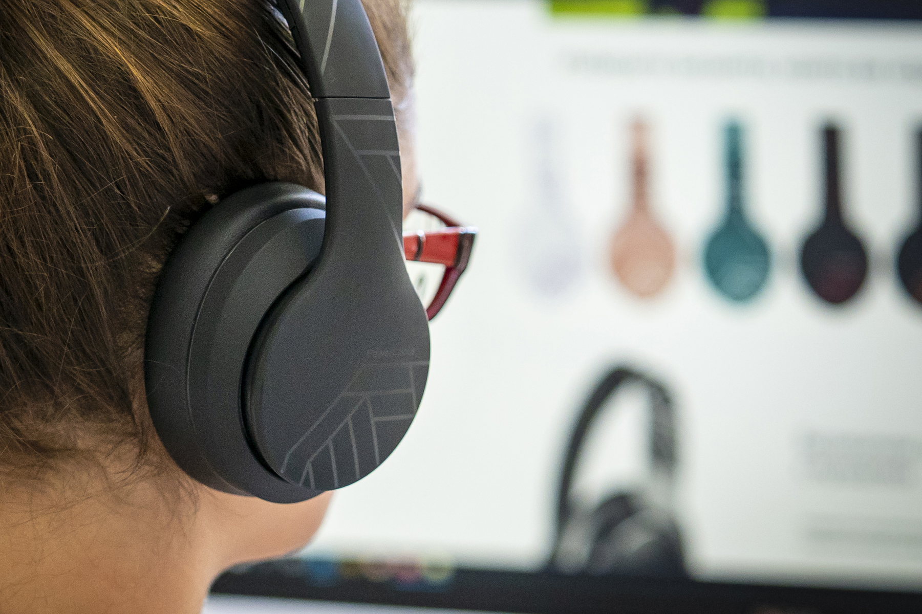 Persona con auriculares negros, gafas rojas, mirando una pantalla. La pantalla muestra auriculares de diferentes colores.