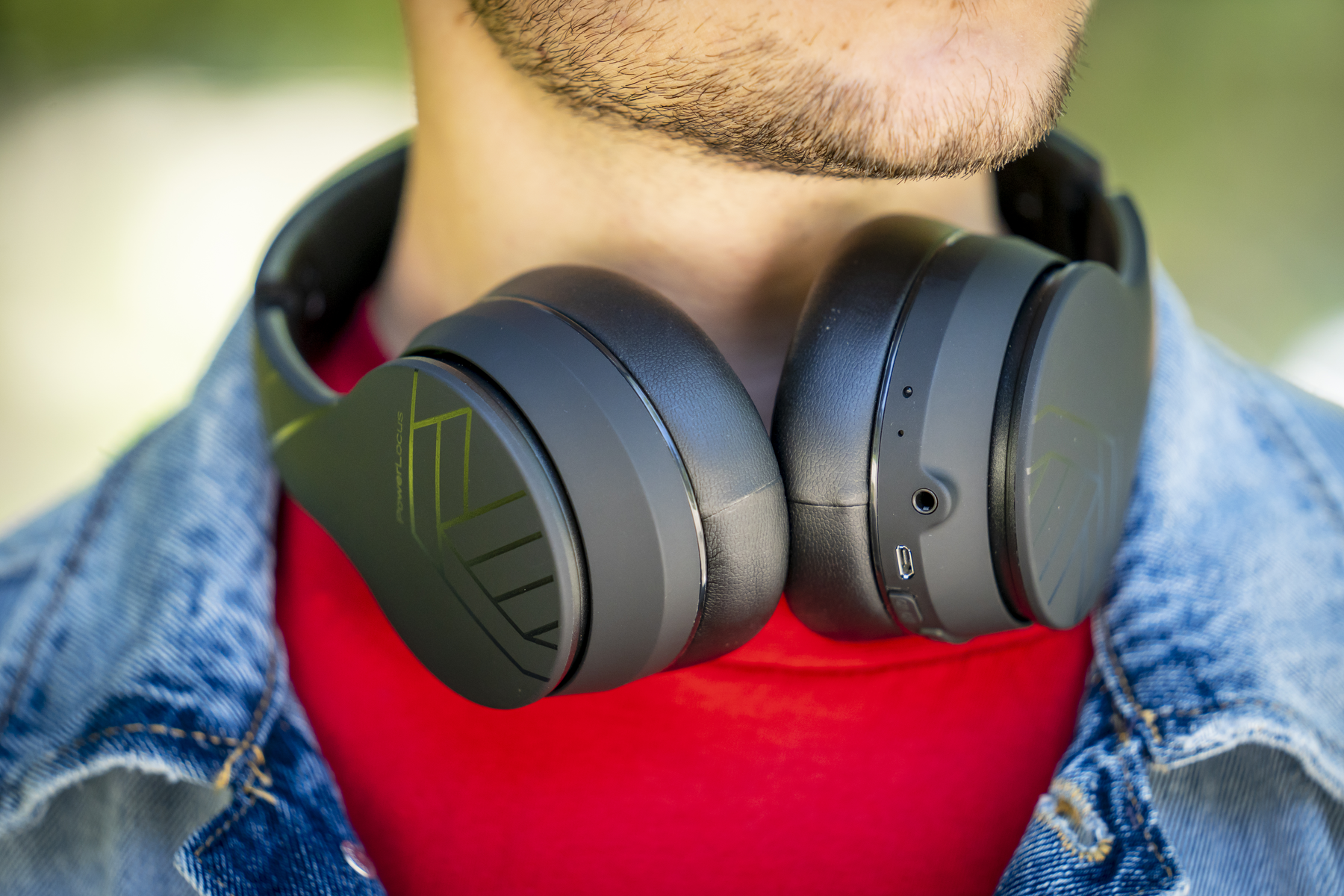 Una persona con auriculares negros alrededor del cuello. Lleva una camisa roja y una chaqueta vaquera. Se ve una barba.
