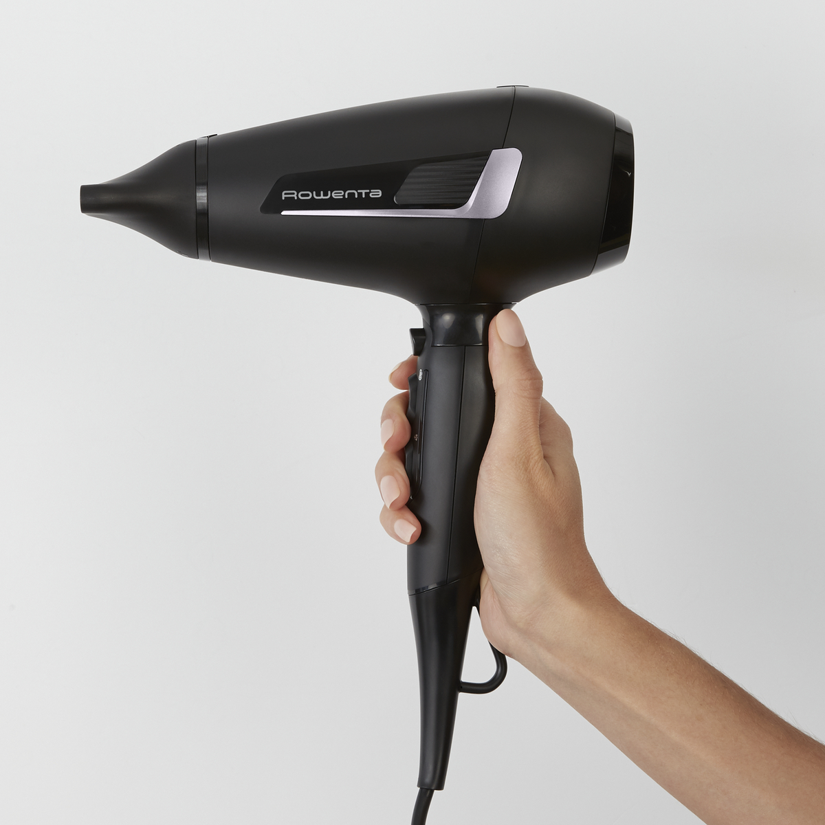 Czarna suszarka do włosów trzymana jest w dłoni na białym tle. Na suszarce widnieje nazwa marki Rowenta.