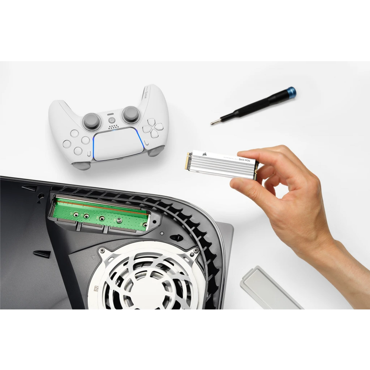 Osoba trzyma srebrny dysk SSD obok konsoli PS5. Na białej powierzchni widoczne są również kontroler i śrubokręt.