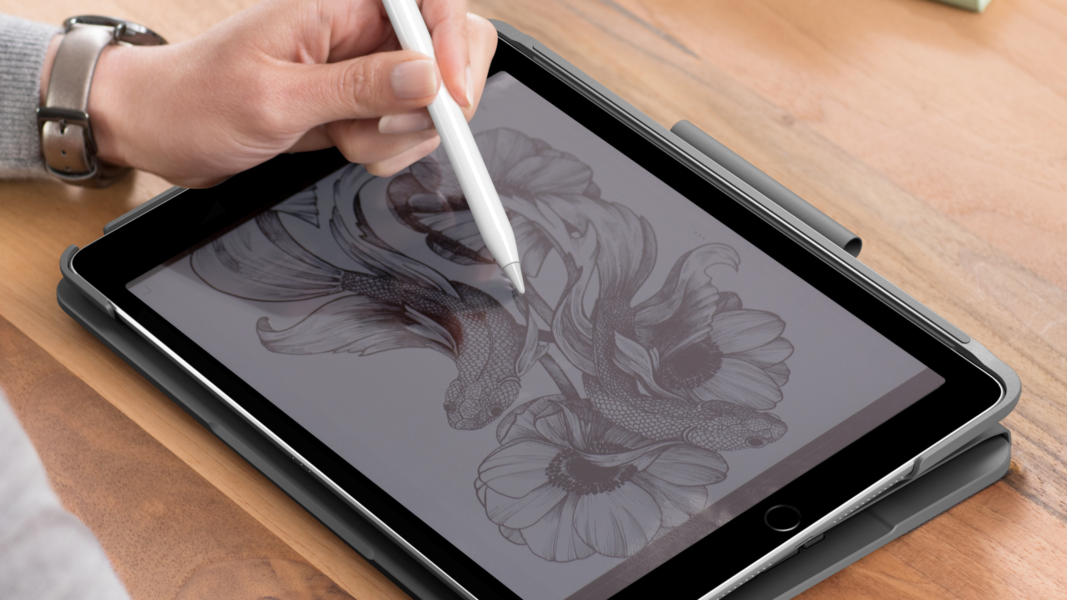 Ręka z rysikiem rysuje na tablecie. Ekran wyświetla rysunek kwiatów i ryb. Na nadgarstku znajduje się zegarek.