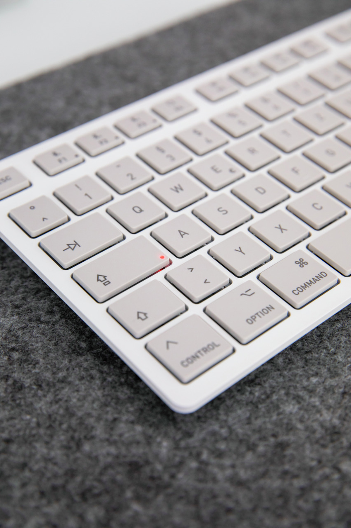 Un teclado de computadora blanco con teclas gris claro está sobre una superficie de fieltro gris oscuro. El teclado está en ángulo hacia arriba.