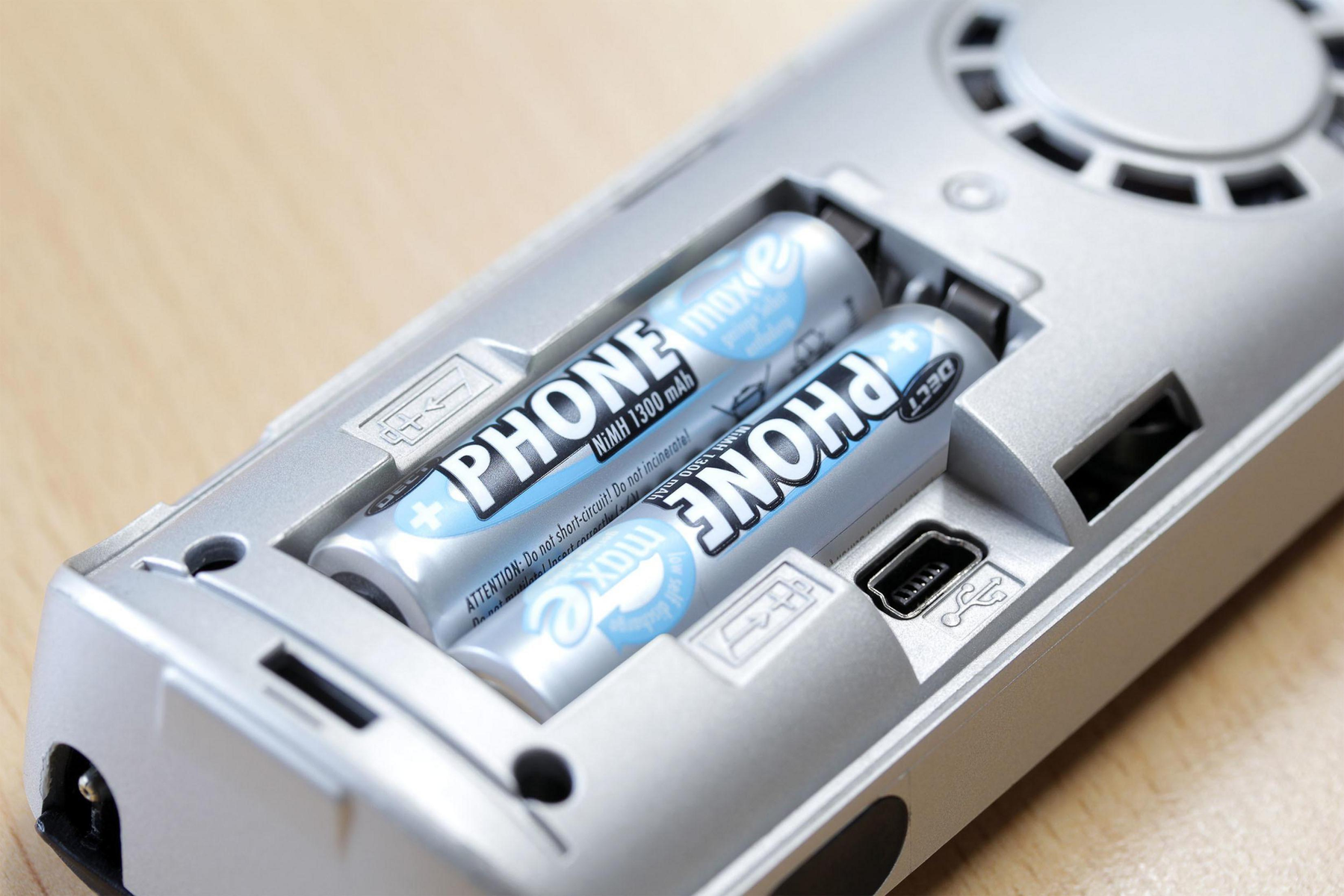Dos baterías etiquetadas 'PHONE' en un dispositivo plateado. El dispositivo tiene un puerto USB y un ventilador. El fondo es una superficie de madera.