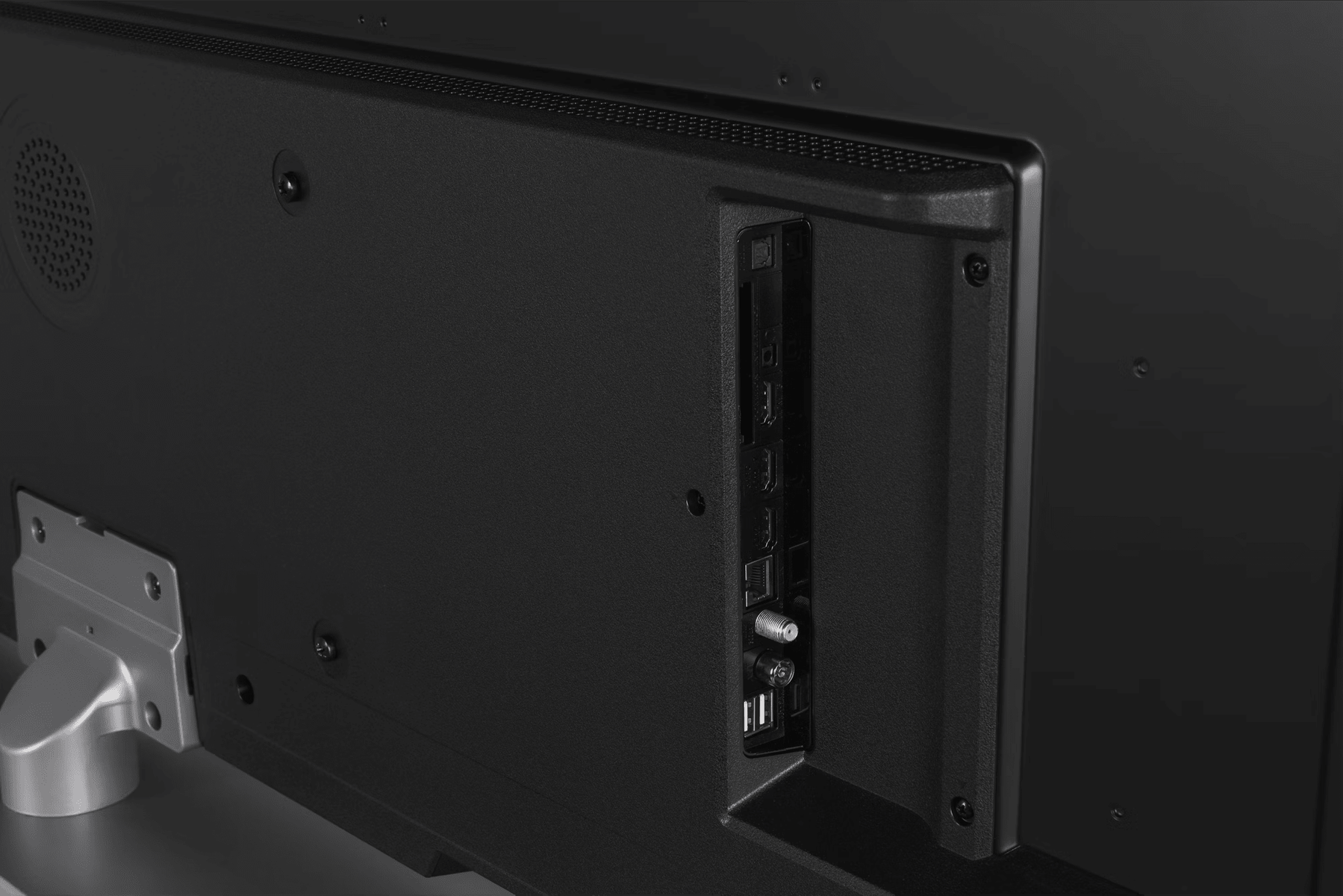 Primer plano de la parte trasera de un televisor negro. Los puertos visibles incluyen HDMI, USB y conexiones de antena. También hay un soporte de montaje plateado.