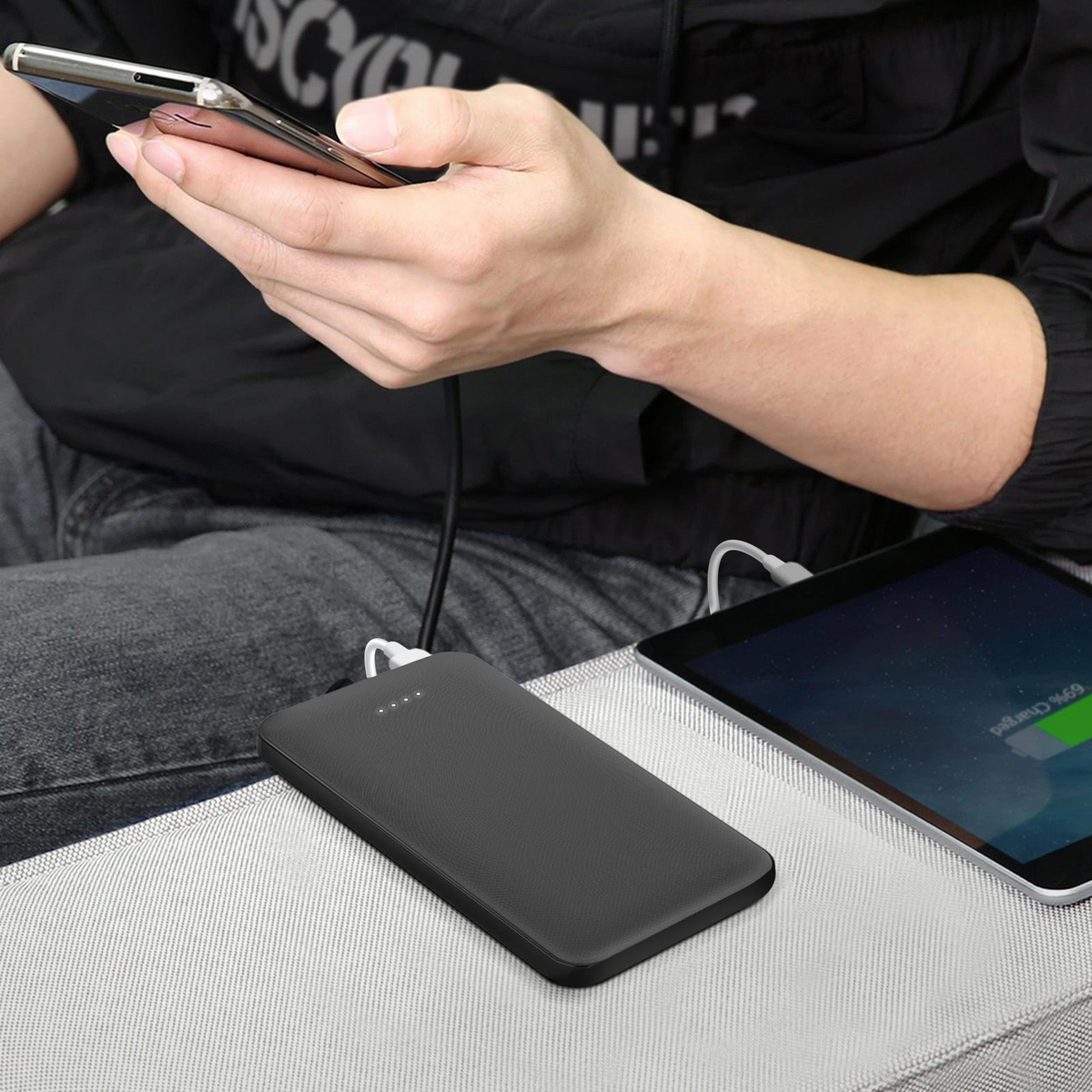 Eine Person hält ein Telefon, das mit einer Powerbank und einem Tablet verbunden ist, alles auf einer grauen Oberfläche, die aufgeladen wird. Das Tablet zeigt 69 % geladen an.