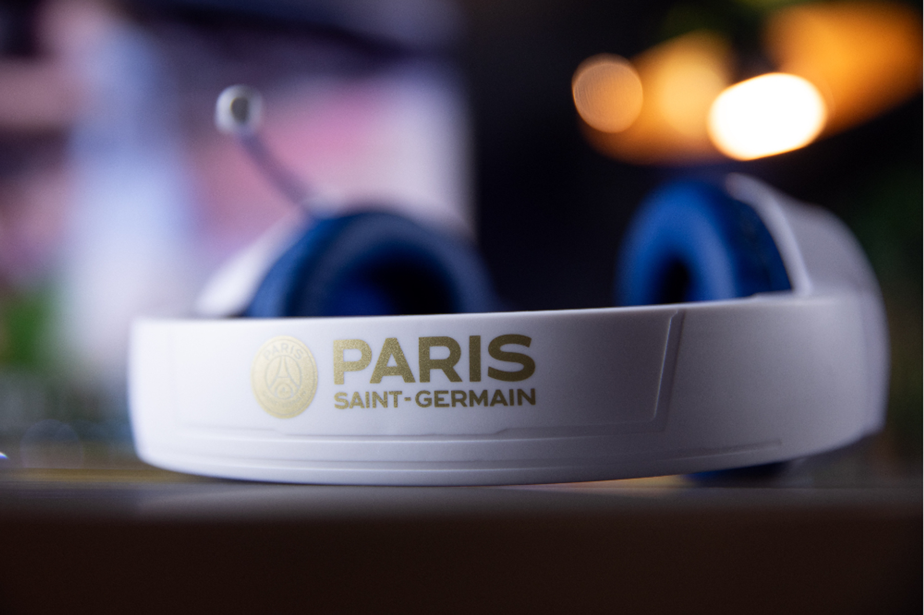 Biało-niebieski zestaw słuchawkowy ze złotym logo 'Paris Saint-Germain'. Ostrość na pałąku. Rozmyte tło.
