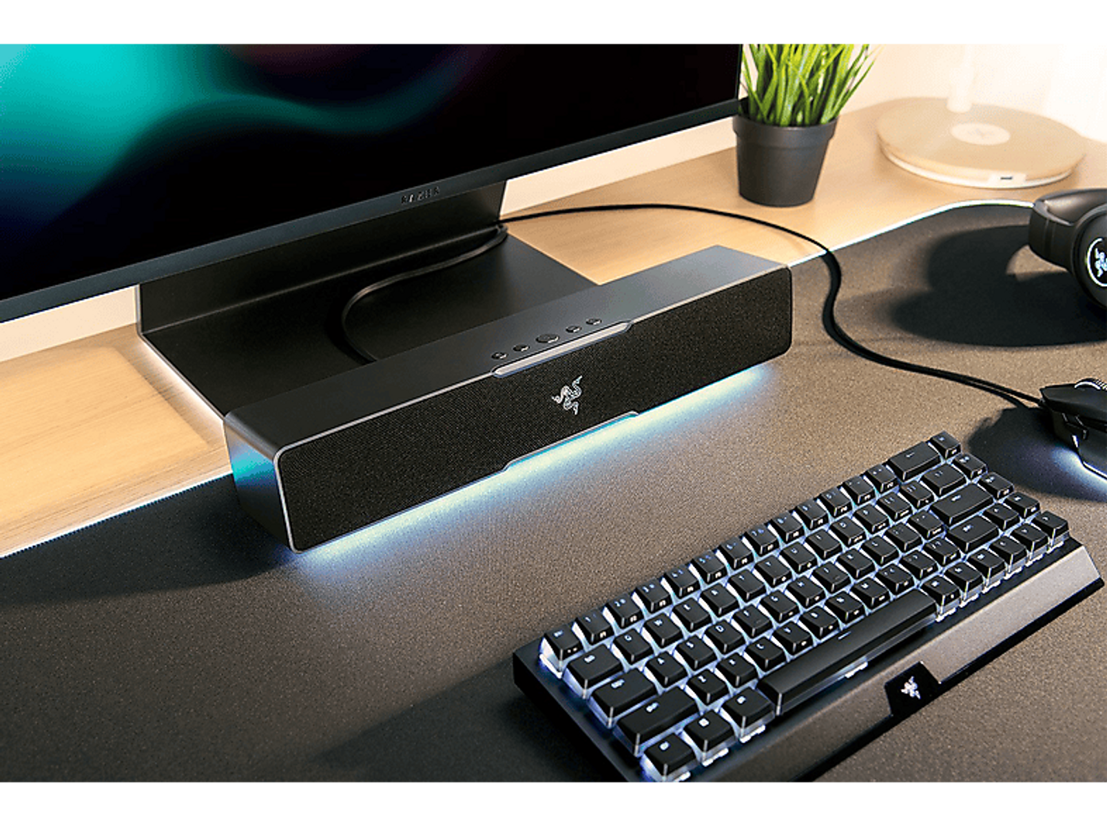 Konfiguracja do gier z monitorem, głośnikiem, klawiaturą i myszą. Głośnik ma logo Razer, a klawiatura podświetlane klawisze.