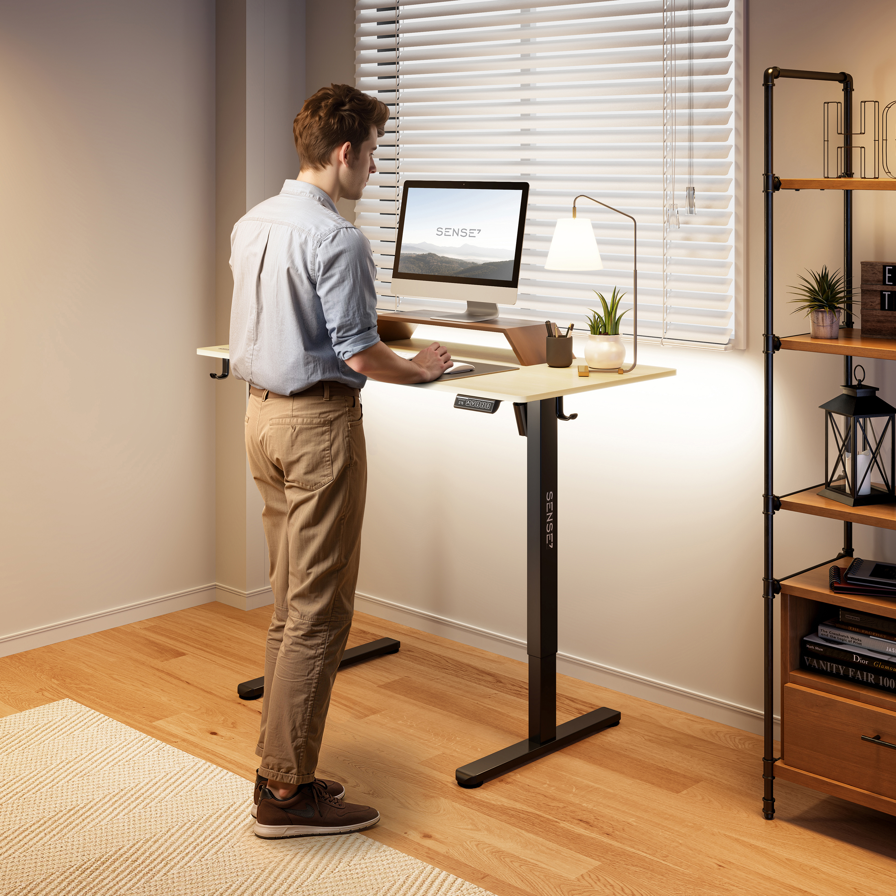 Un uomo in piedi a una scrivania. Un monitor, una lampada e una piccola pianta sono sulla scrivania. Scaffali contengono libri e decorazioni.