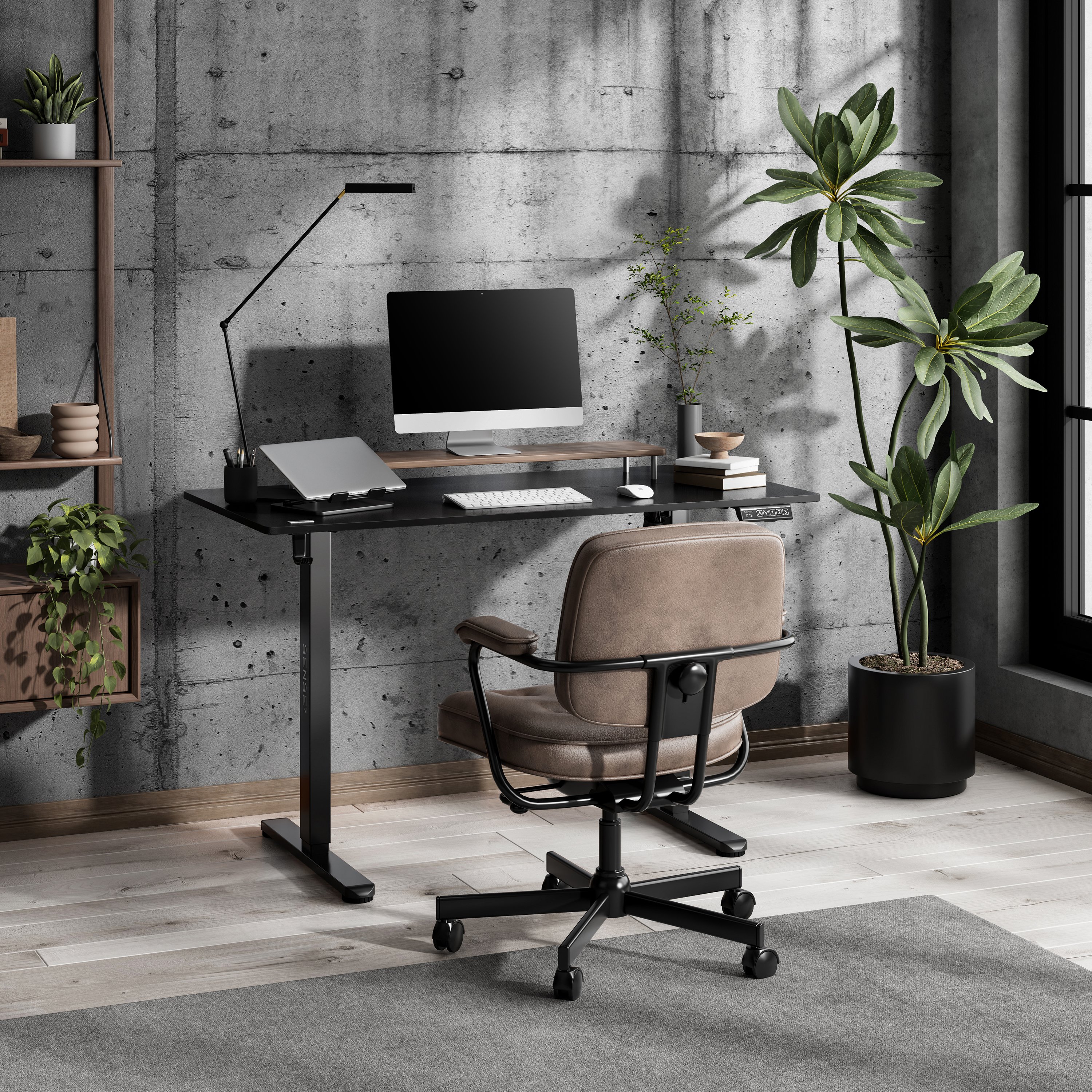 Moderne kantooropstelling met een zwarte bureau, computer en stoel. Met betonnen muur en planten.