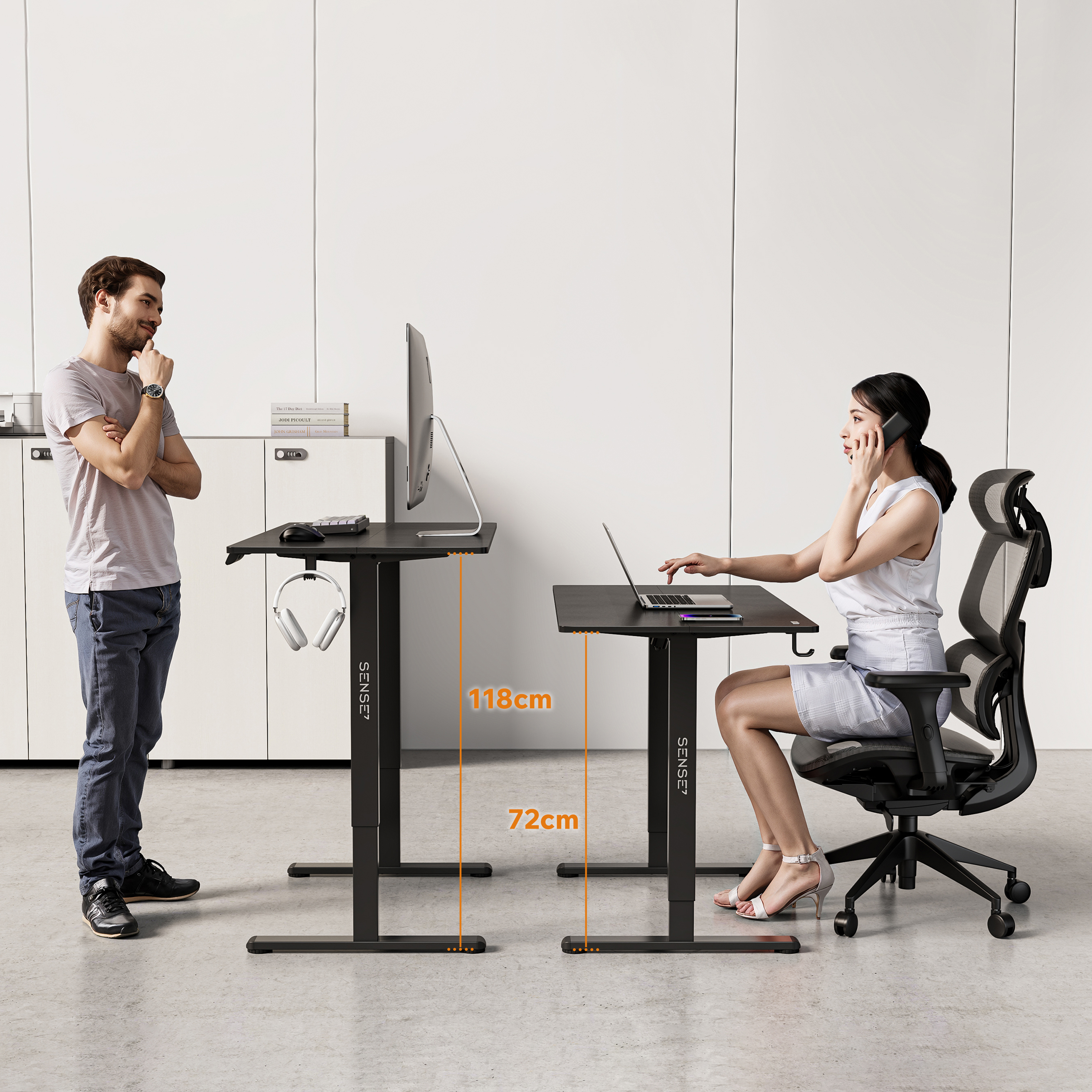 Een man en een vrouw bij in hoogte verstelbare bureaus. Man staat, vrouw zit, gebruikt laptop en telefoon.