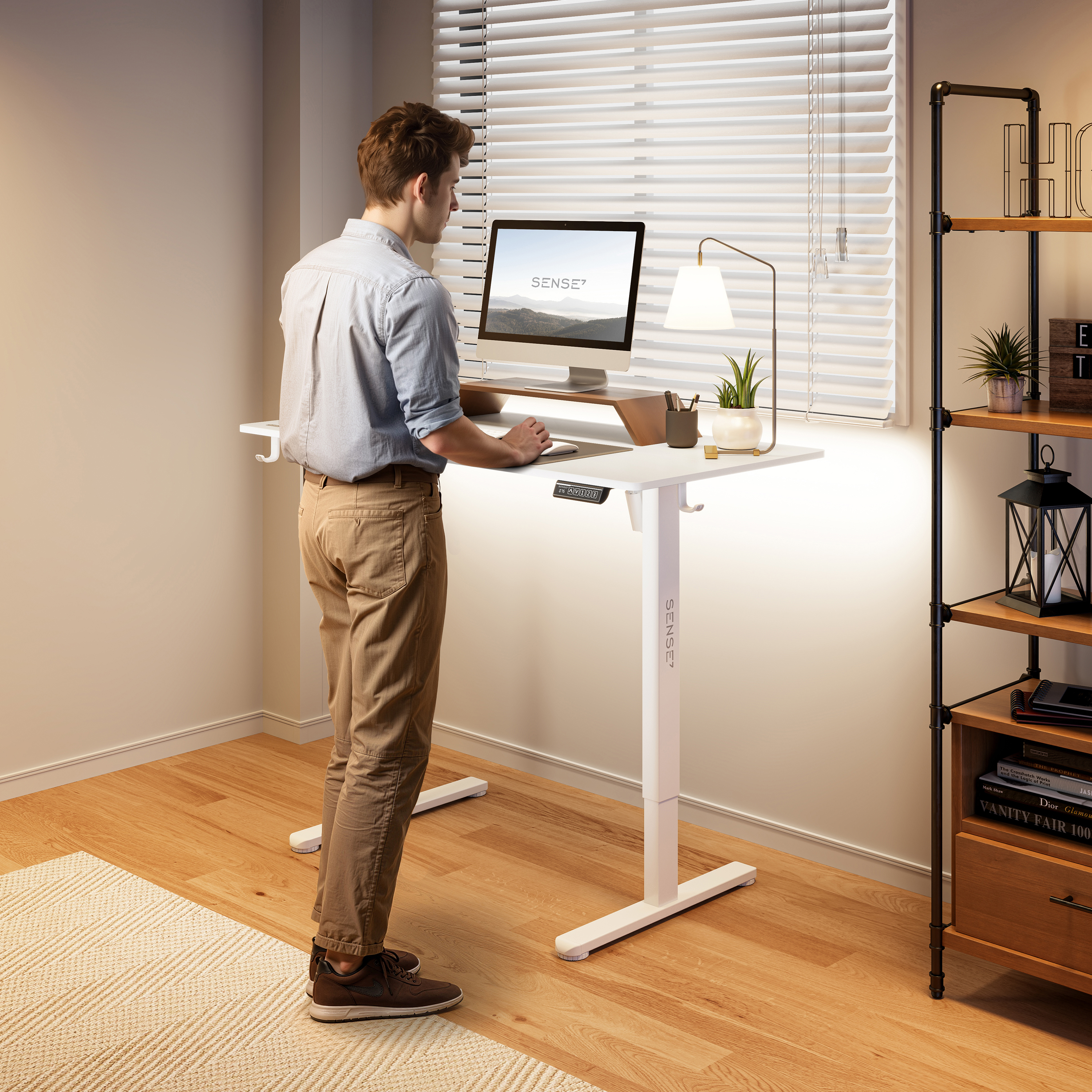 Een man staat aan een witte bureau en werkt op een computer. Een lamp, plant en boekenplank zijn ook zichtbaar.