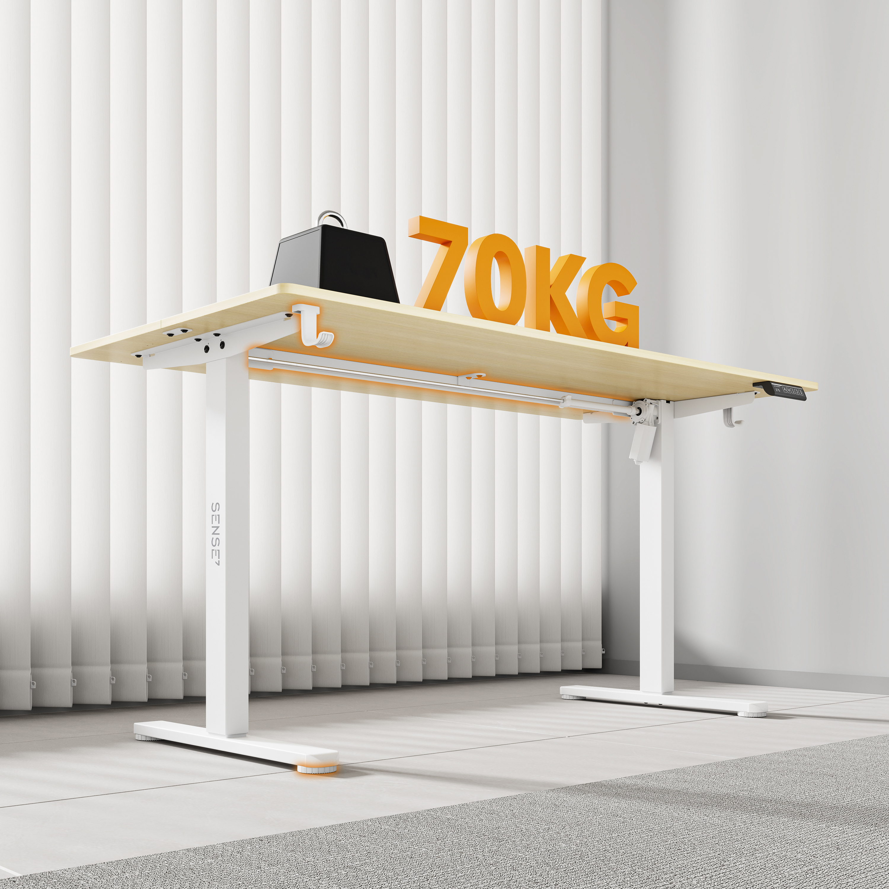 Een in hoogte verstelbaar bureau met een houten blad. Een zwarte doos en oranje letters "70KG" staan erop. Witte jaloezieën zijn zichtbaar.