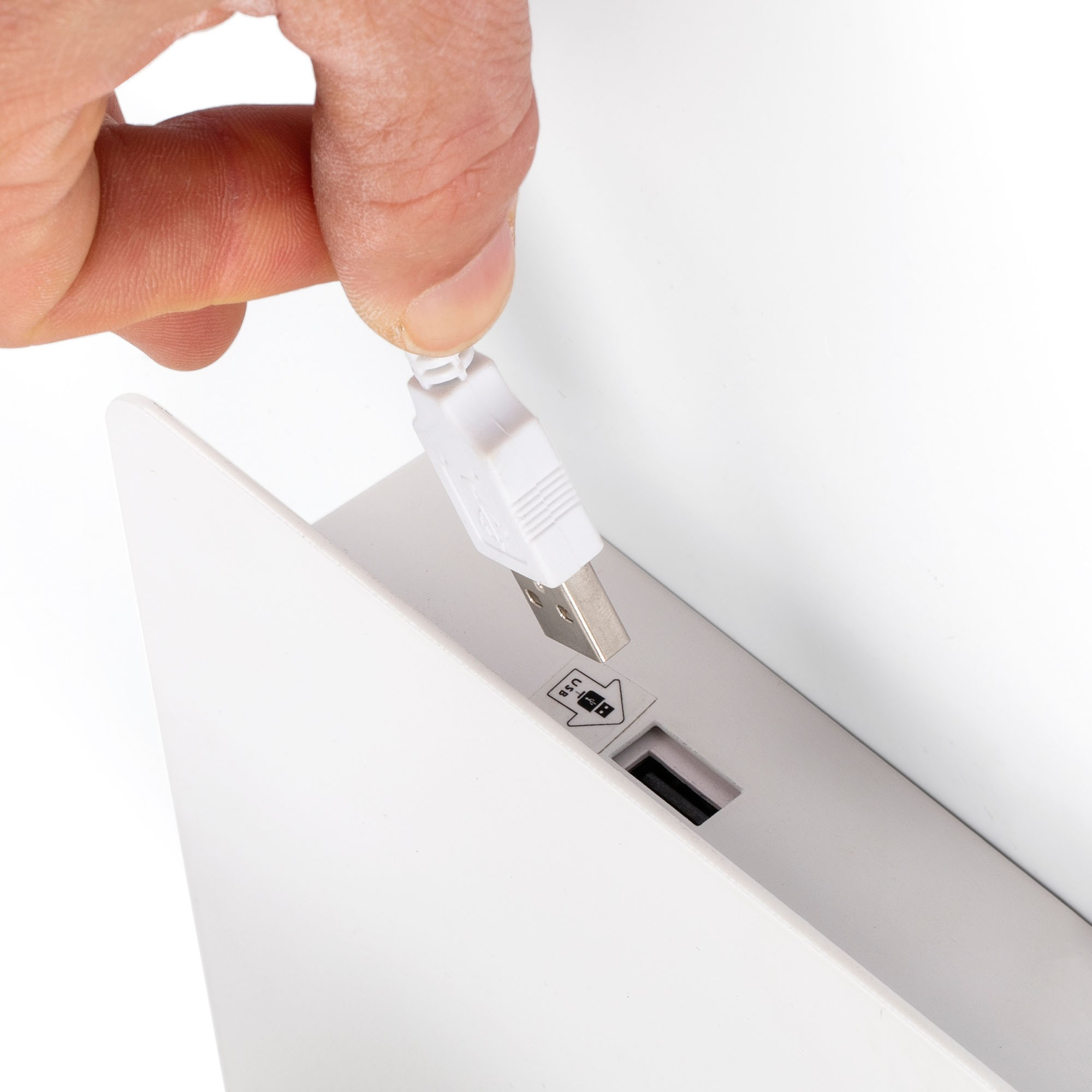 Una mano inserisce un cavo USB bianco in una porta su un dispositivo bianco. La porta ha un simbolo USB.