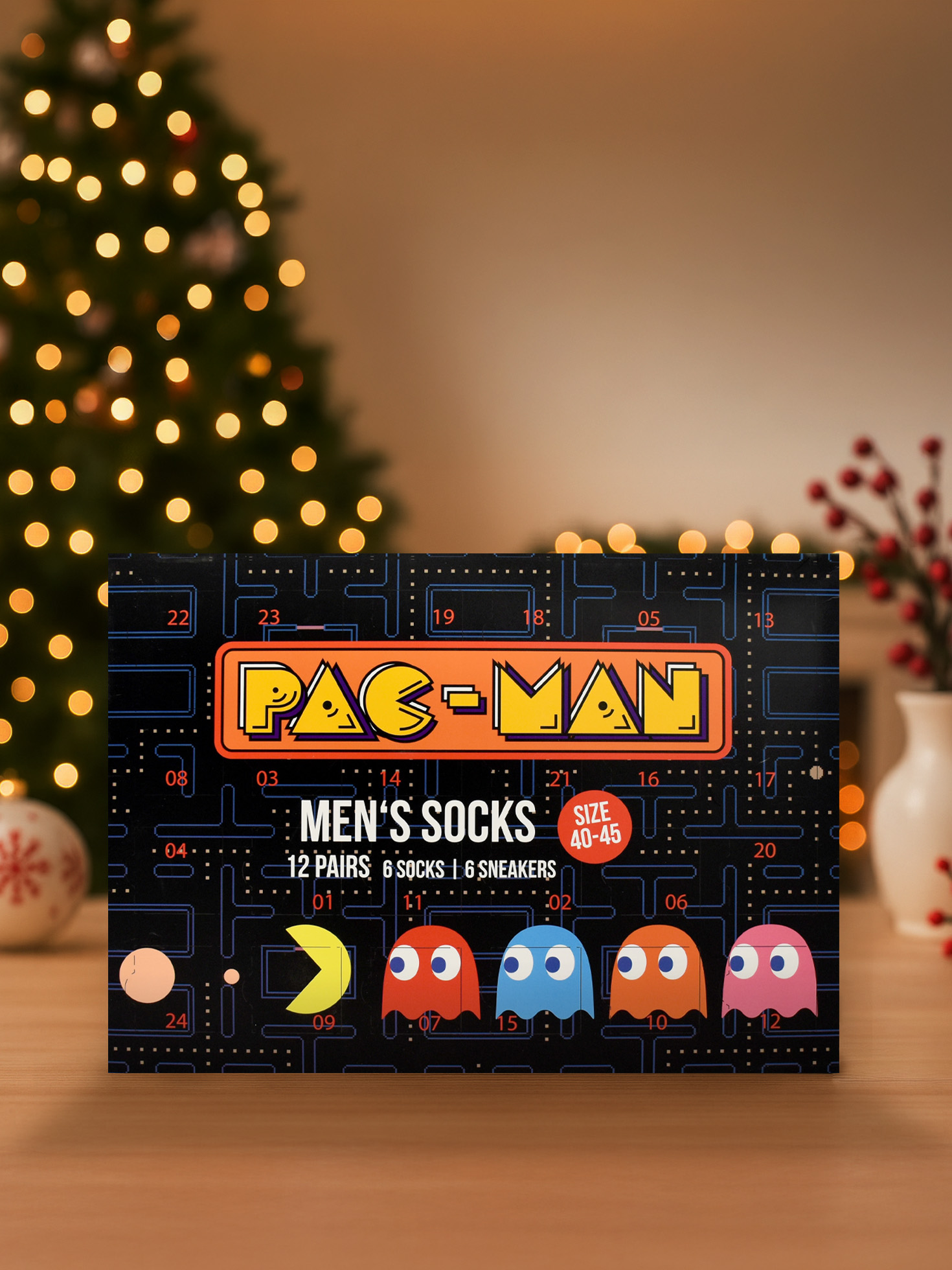 Pac-Man Herrensocken-Box. Weihnachtsbaum im Hintergrund. Die Box hat Pac-Man-Charaktere und Größenangaben.