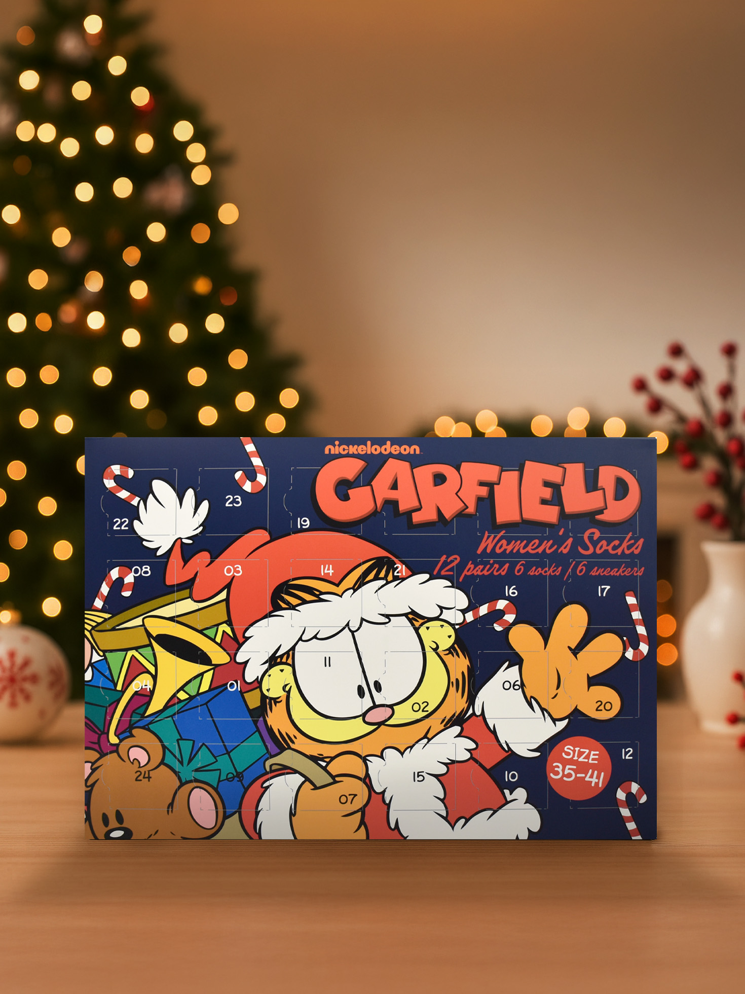 Garfield-Adventskalender mit Socken auf einem Holztisch. Weihnachtsbaum und Vase mit roten Beeren im Hintergrund.