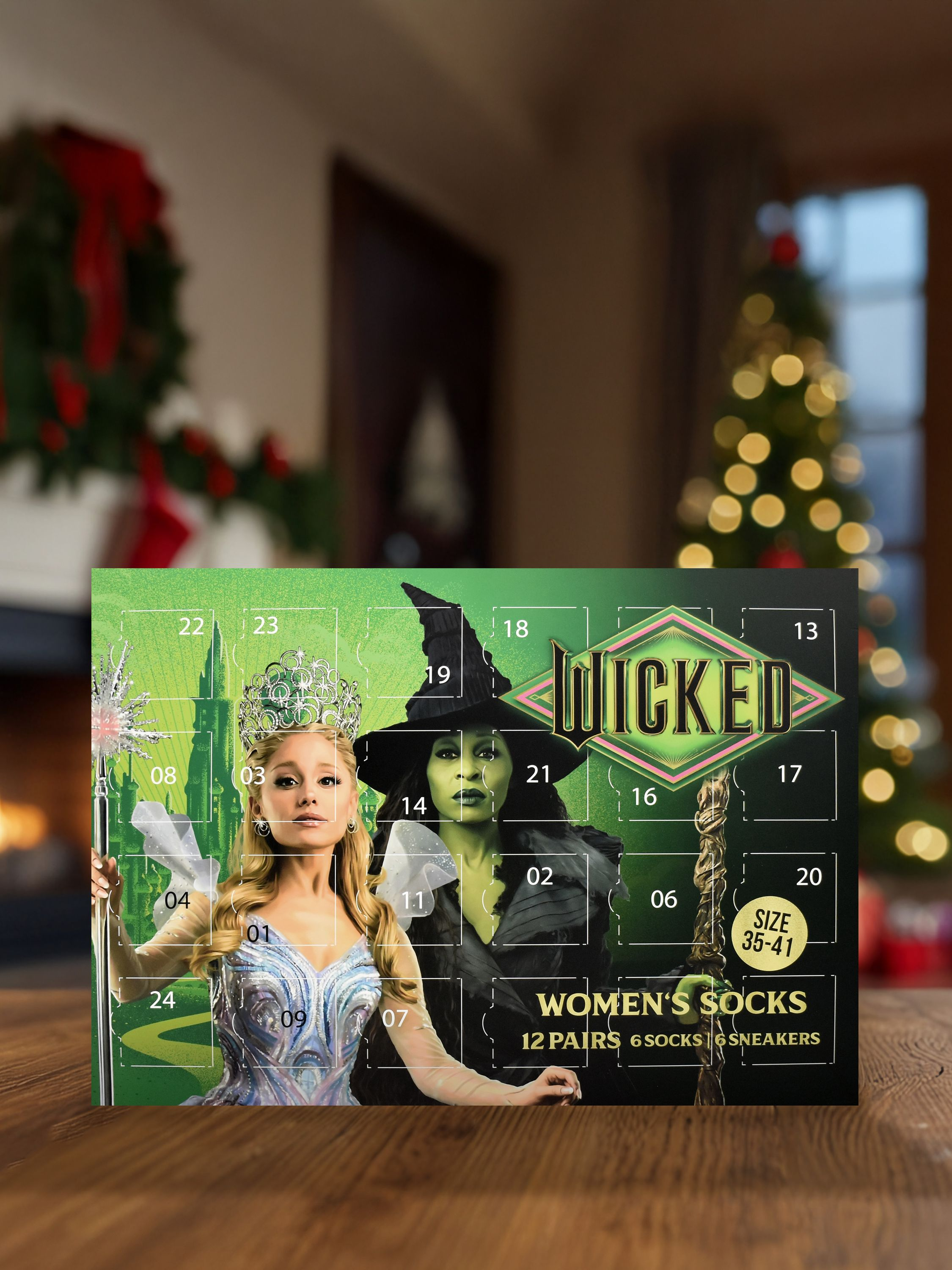 Wicked Adventskalender mit zwei Frauen in Kostümen. Im Hintergrund ist ein Raum mit Weihnachtsbaum und Kranz.